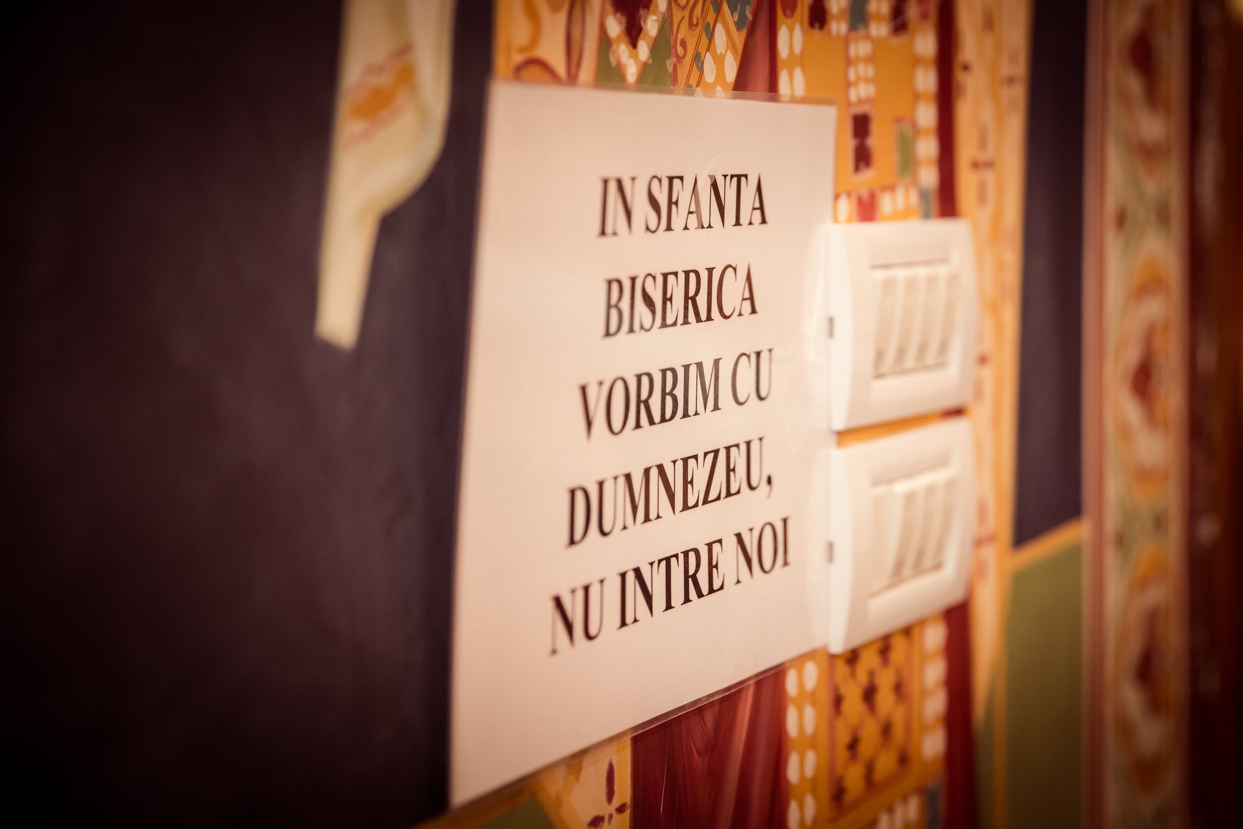 A close-up of a sign with text in a church or religious setting, with colorful stained glass windows in the background.