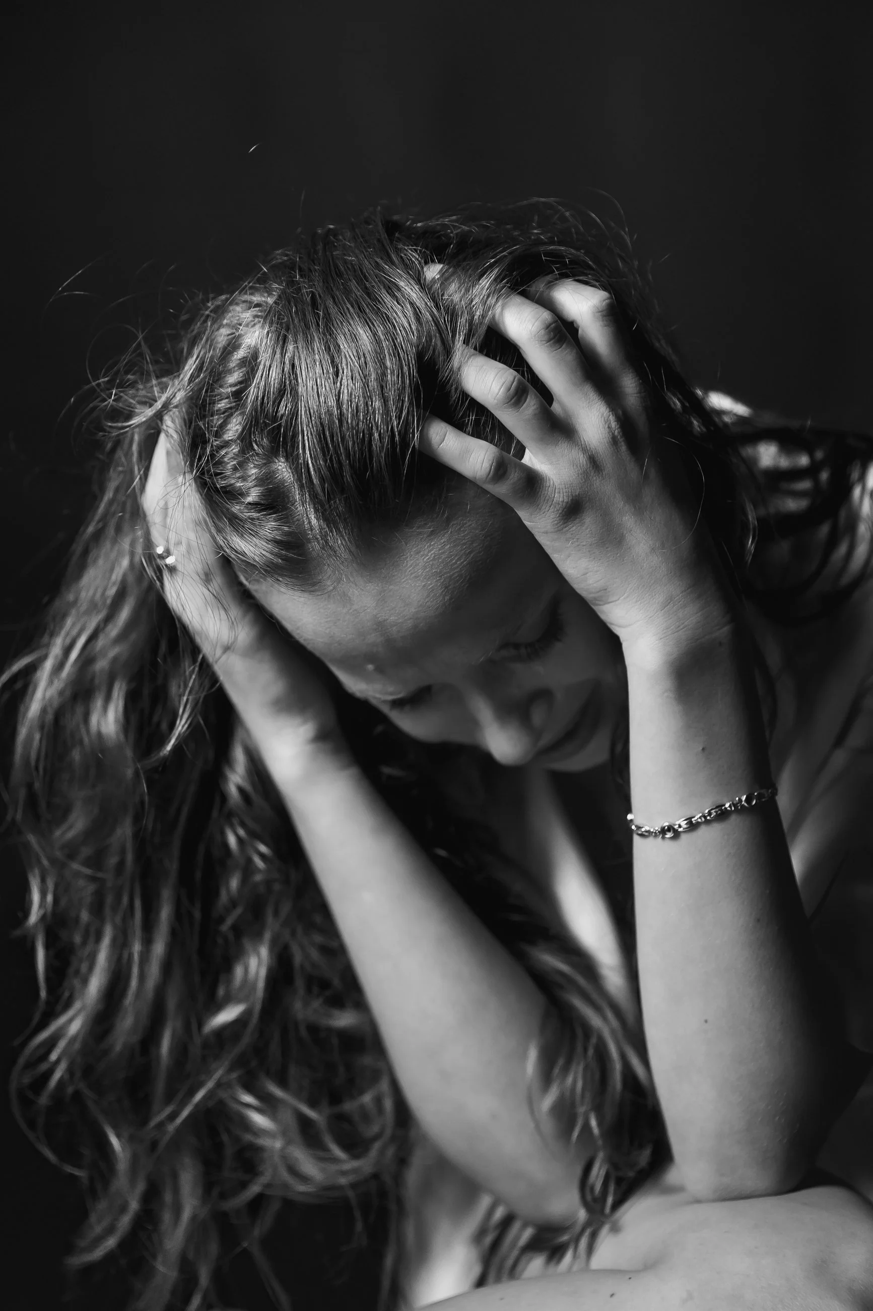 A person with curly hair holding their head with both hands, in a black and white photograph.