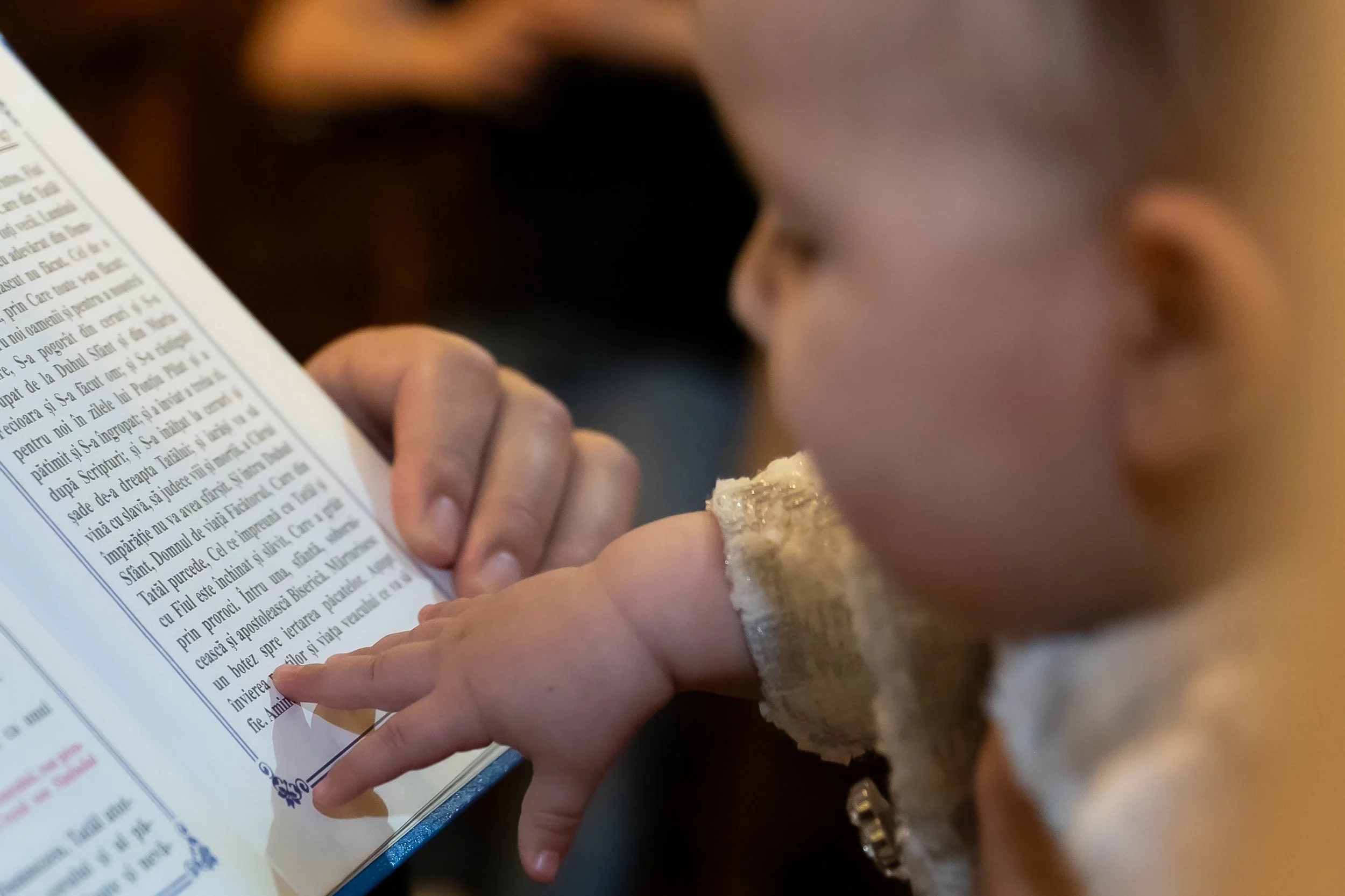 A young girl is holding a piece of bread and reading a book, with her face close to the text, in a close-up view.