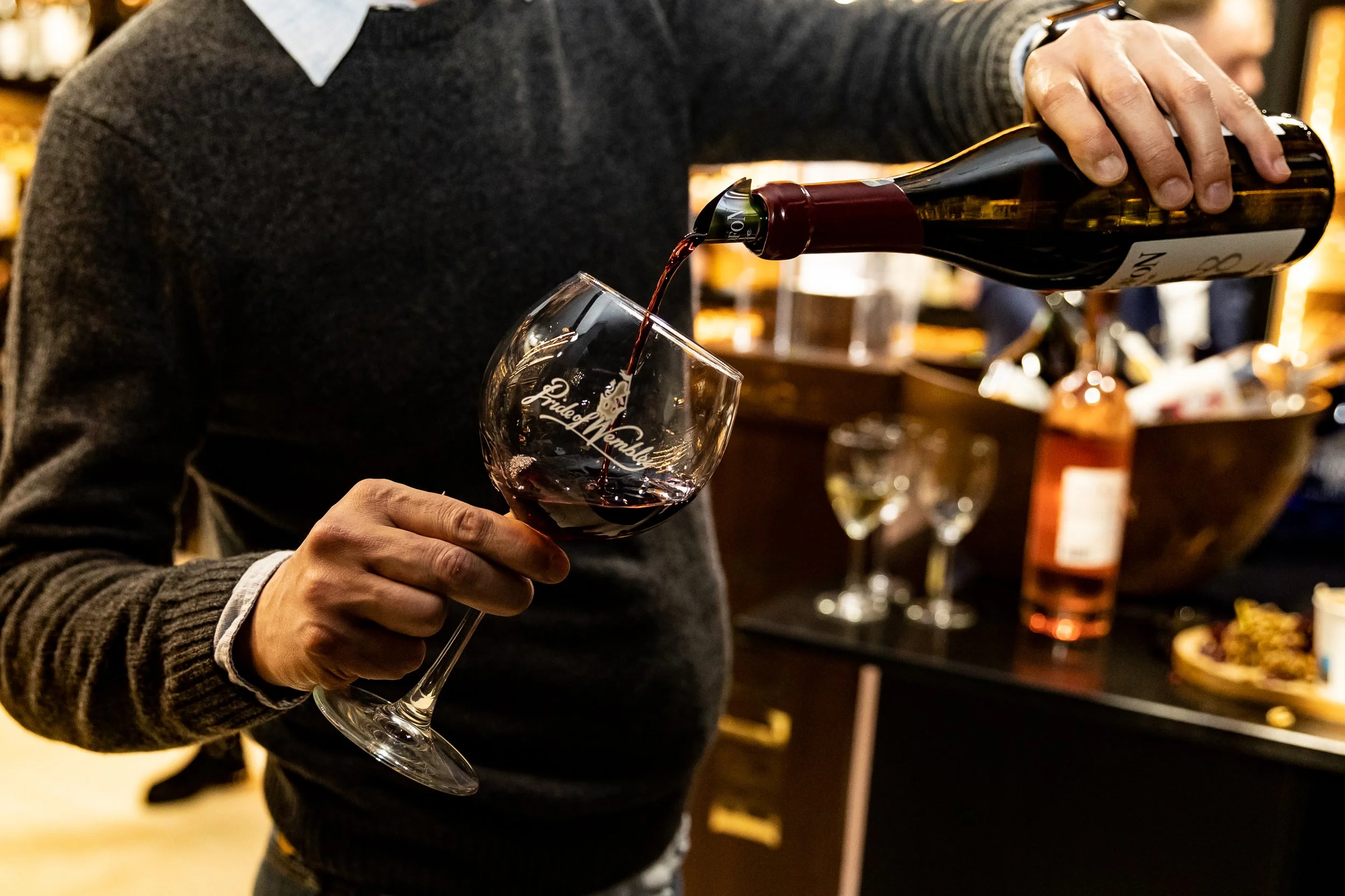 Person pours red wine into a wine glass in a liquor store or wine shop.