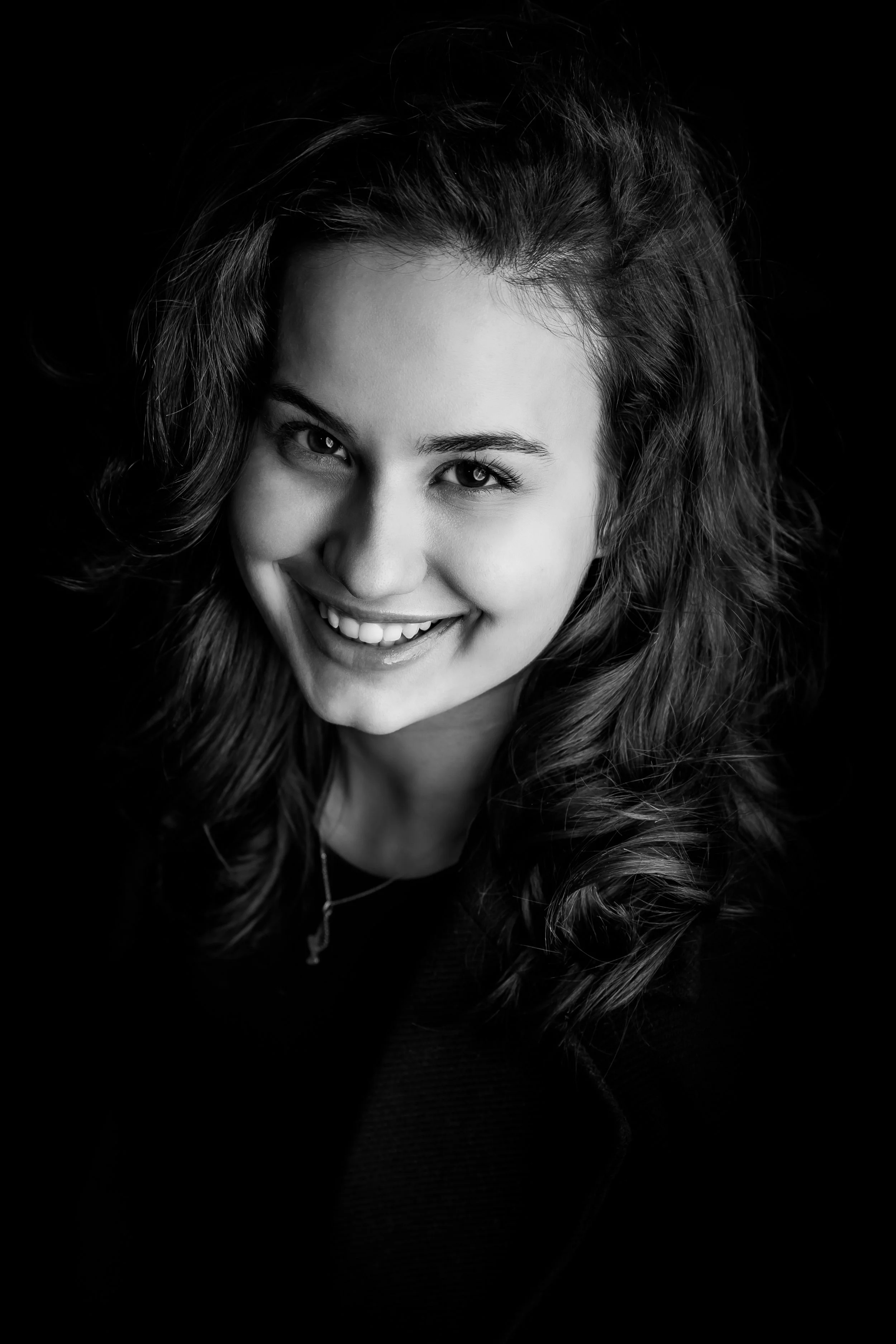 Black and white portrait of a young woman with long, wavy hair smiling and looking at the camera.