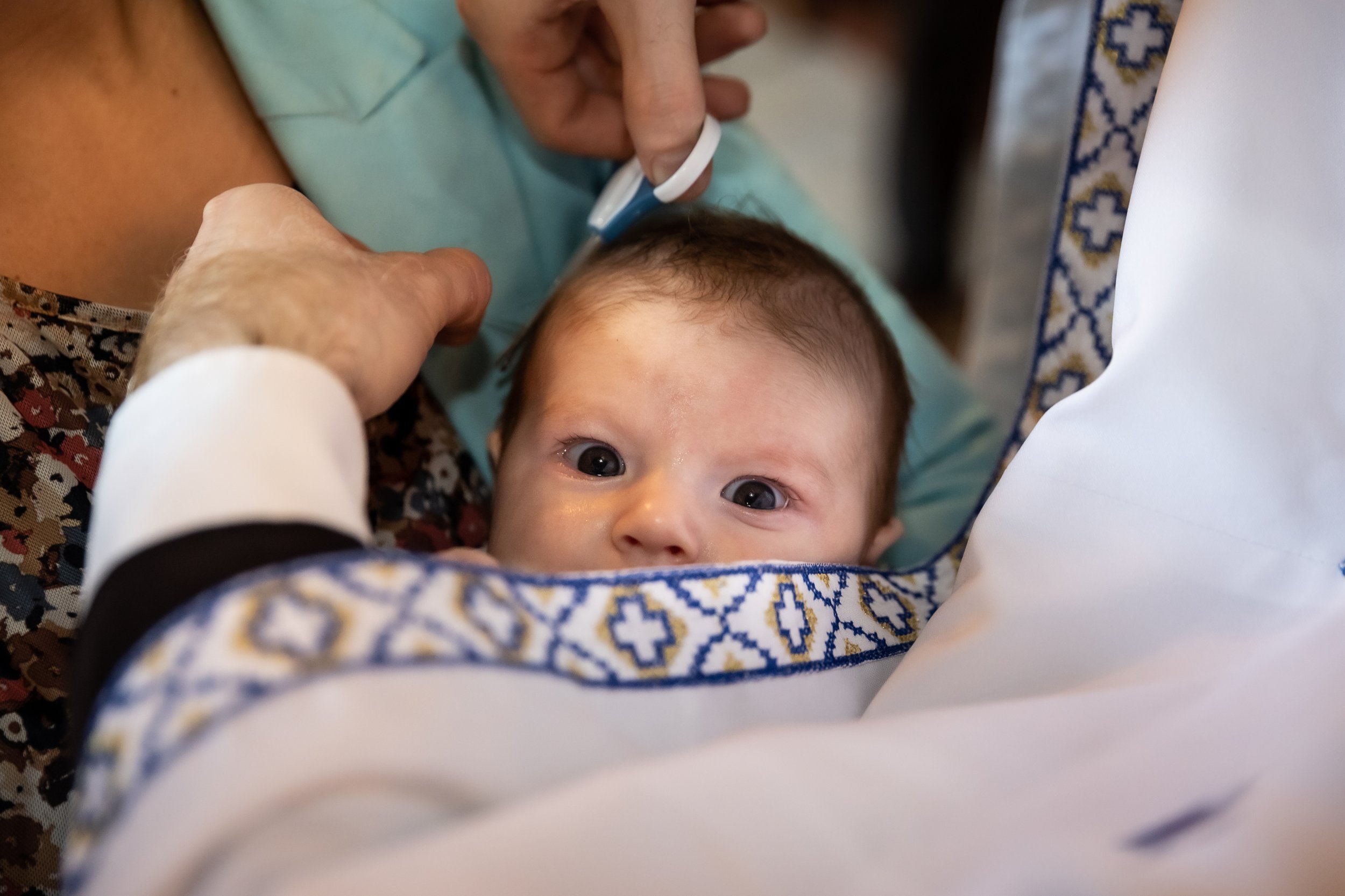 Close-up of a baby with wide eyes lying in a decorated cradle, with hands caring for the baby.