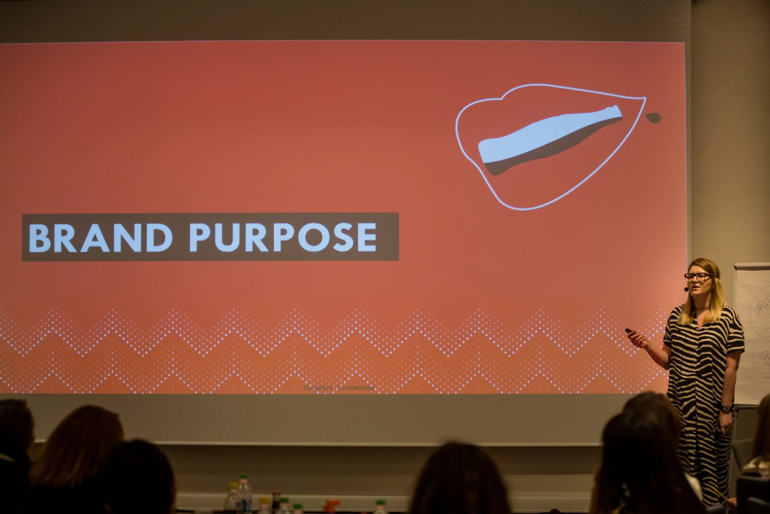 Presentation slide titled 'Brand Purpose' with a graphic of a shoe outline and a paint stroke inside it, and a woman in striped shirt speaking in front of an audience.