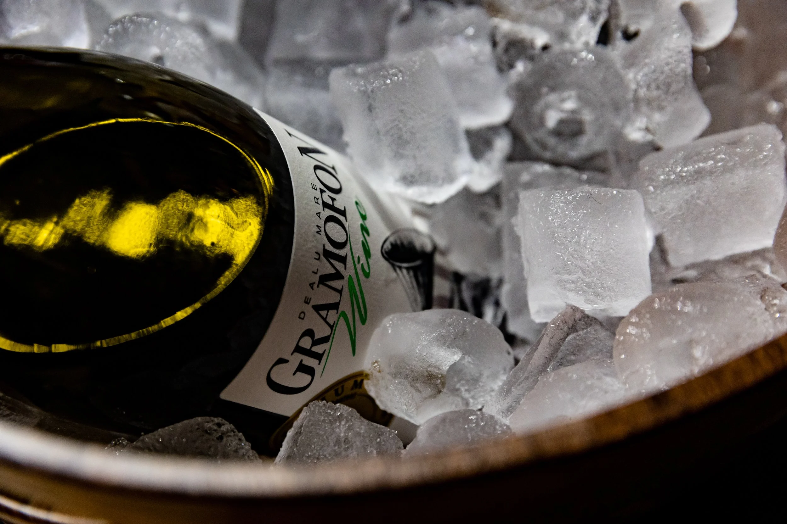 A wine bottle lying on its side in a container filled with ice cubes.