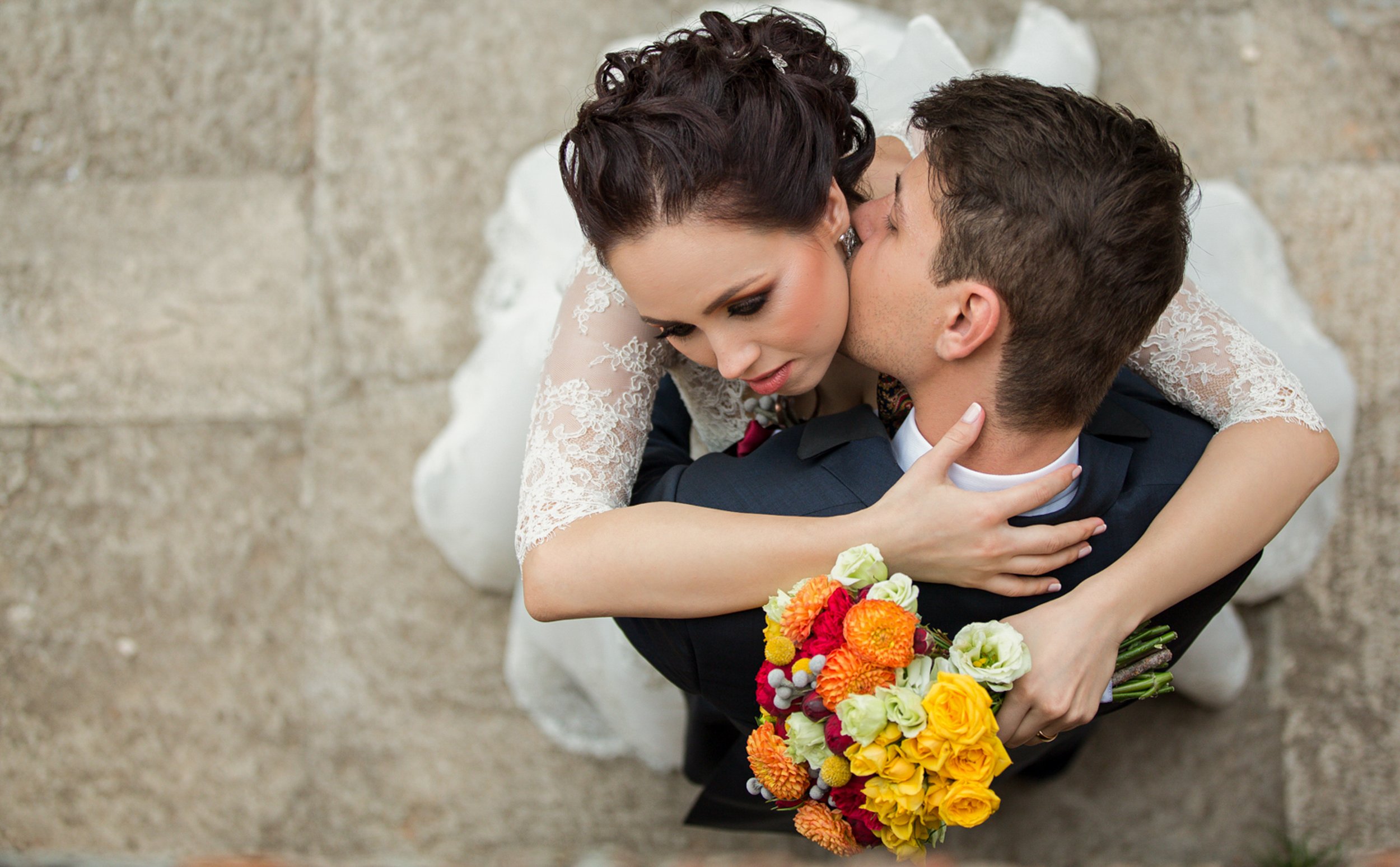 A bride and groom hugging, with the bride holding a colorful bouquet of flowers.