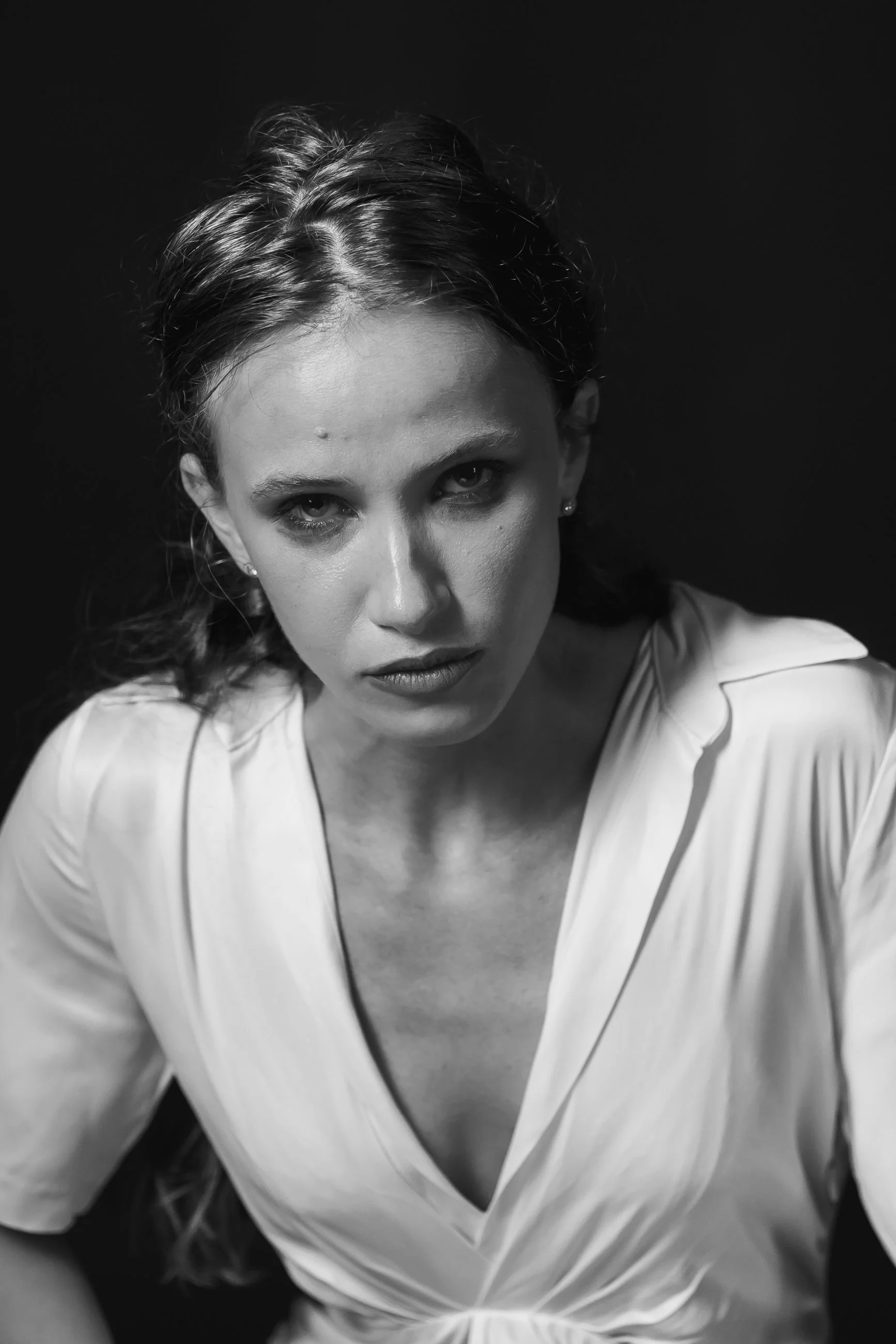 Black-and-white close-up portrait of a woman with sea-green eyes and dark, voluminous hair, wearing a white blouse with an open collar, against a dark background.