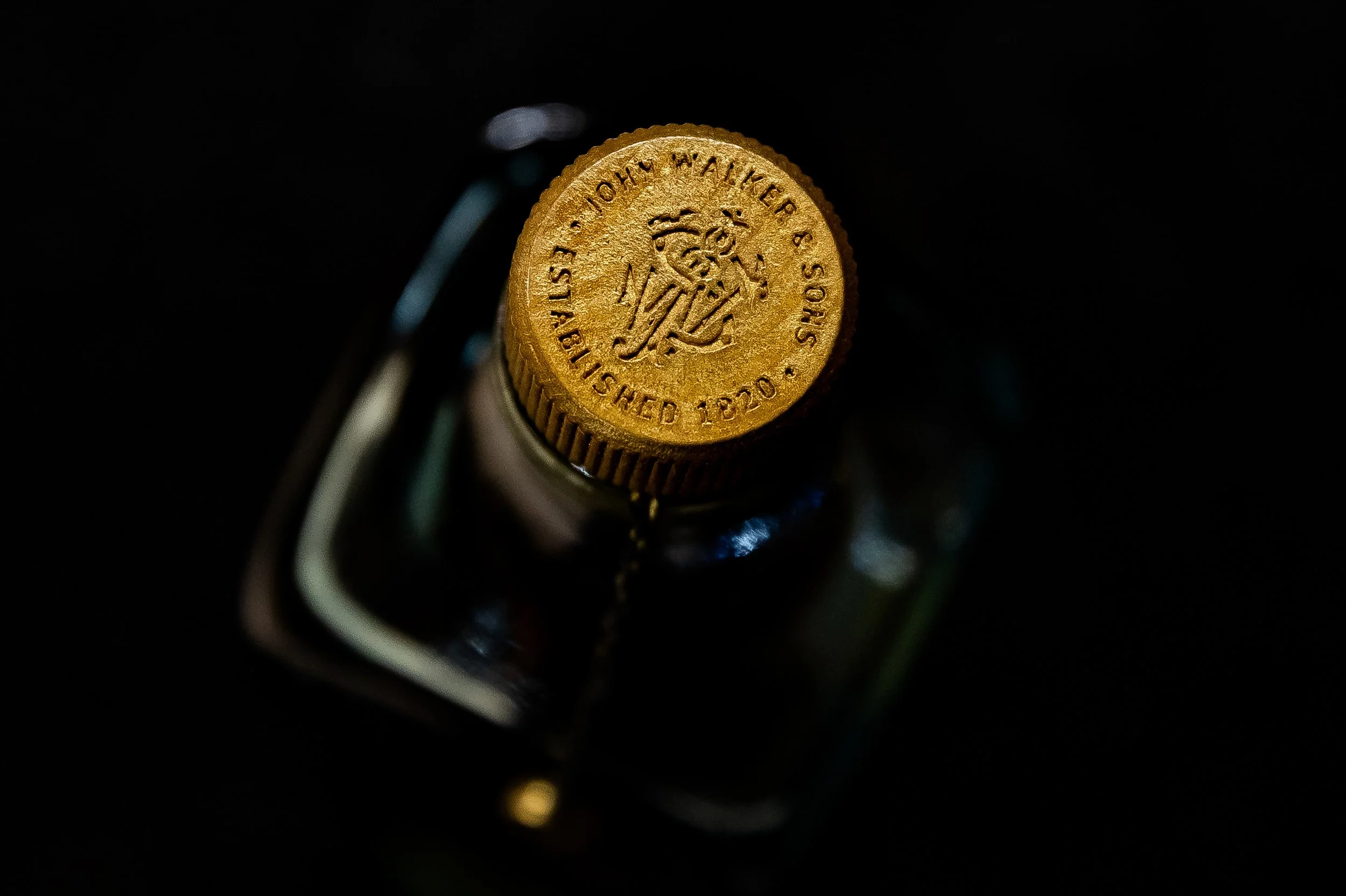 Close-up of a gold-colored bottle cap with engraved text, partially visible, on a dark background.