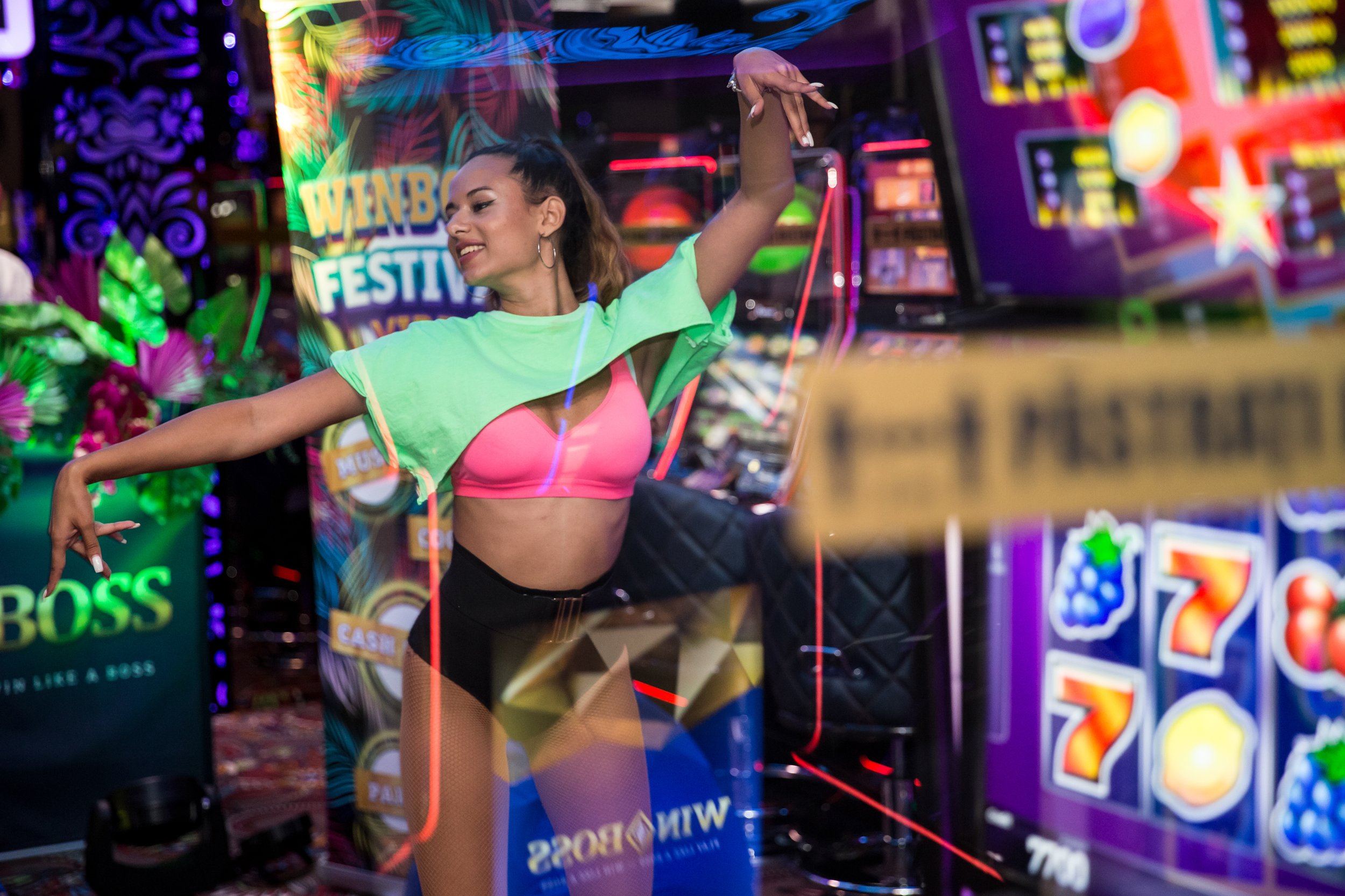 A young woman dancing in front of a colorful, neon-lit arcade with bright signs and gaming machines.