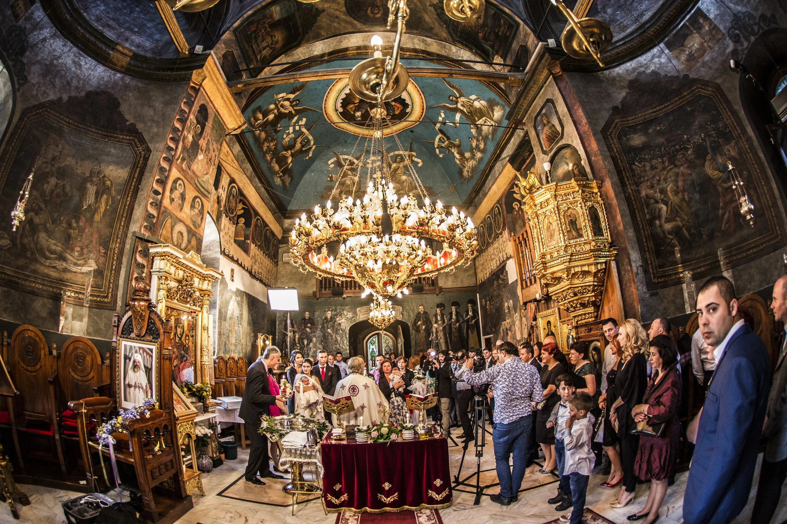 People attending a religious ceremony or event inside a church with ornate gold decorations, religious iconography, and a chandelier hanging from the ceiling.