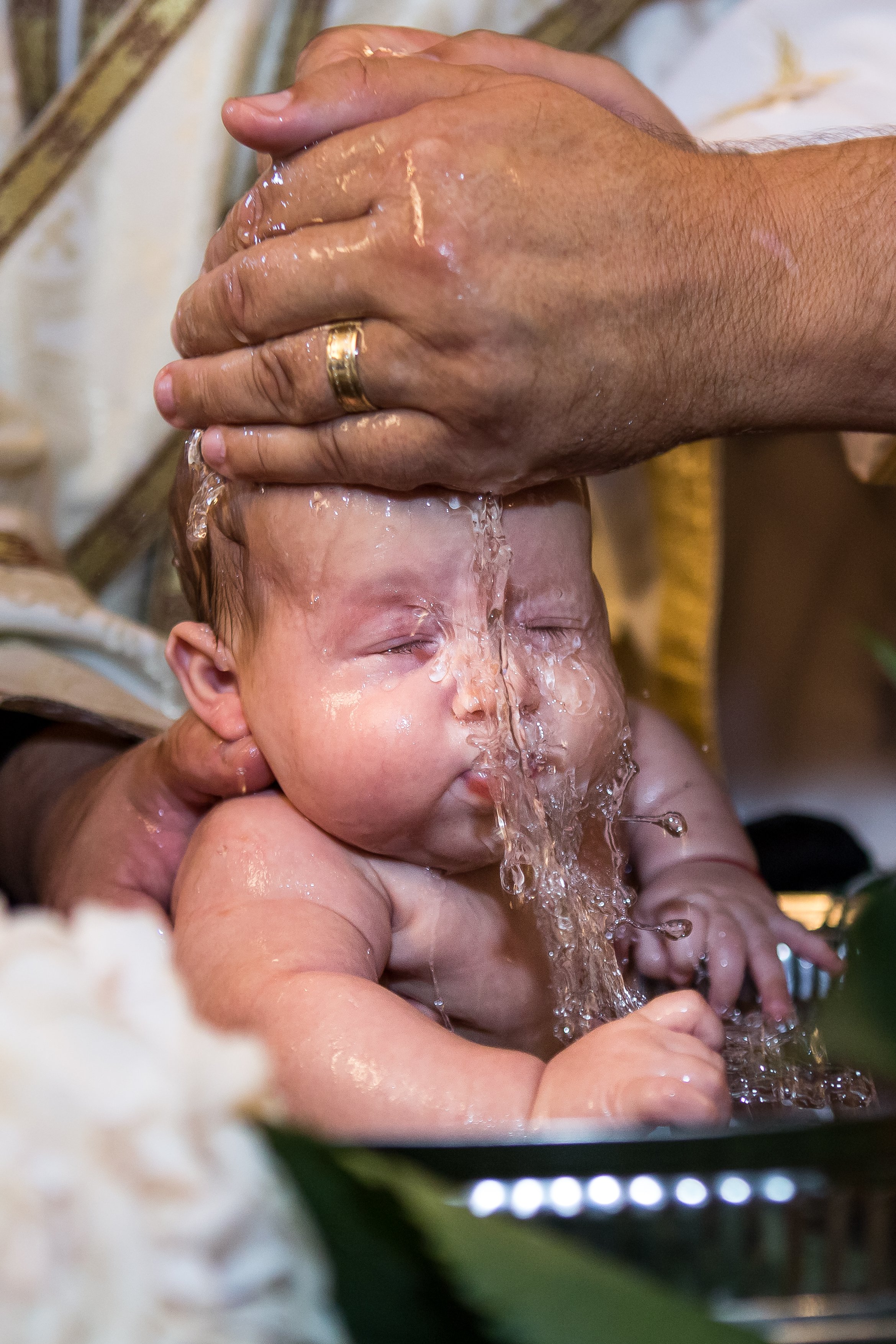 A person is holding a baby during a water baptism ceremony, pouring water over the baby's head.