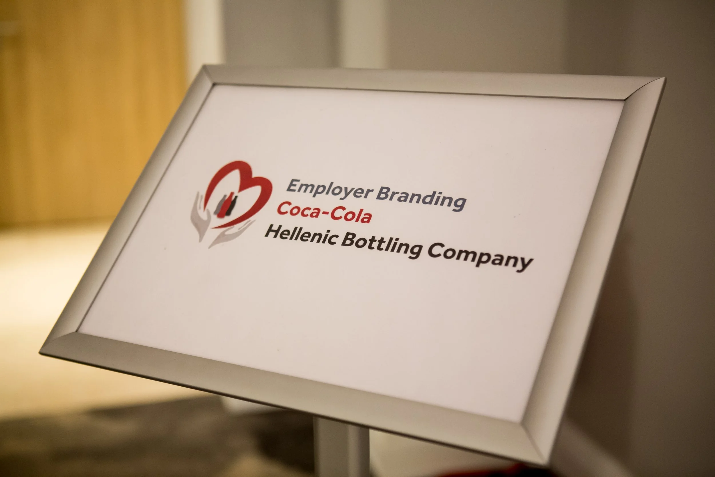 A framed sign displaying the text 'Employer Branding Coca-Cola Hellenic Bottling Company' with the Coca-Cola logo.