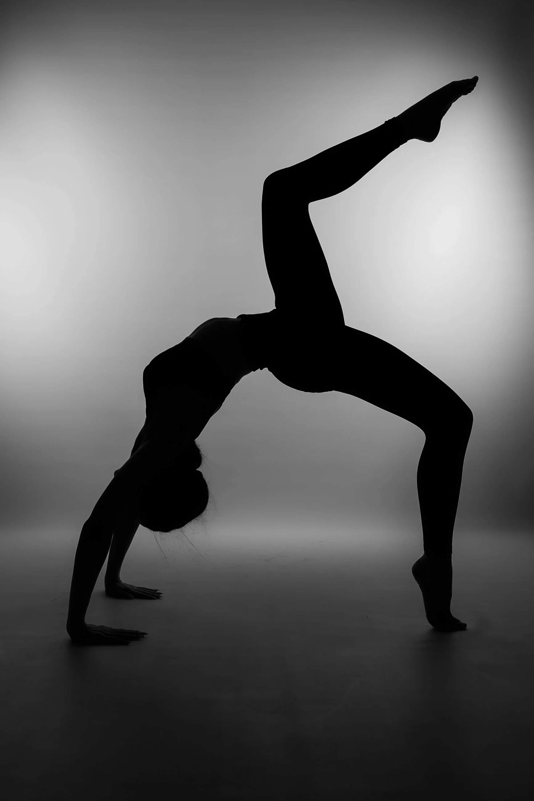 Silhouette of a person performing a yoga pose in a headstand with legs extended in a V-shape against a gradient background.