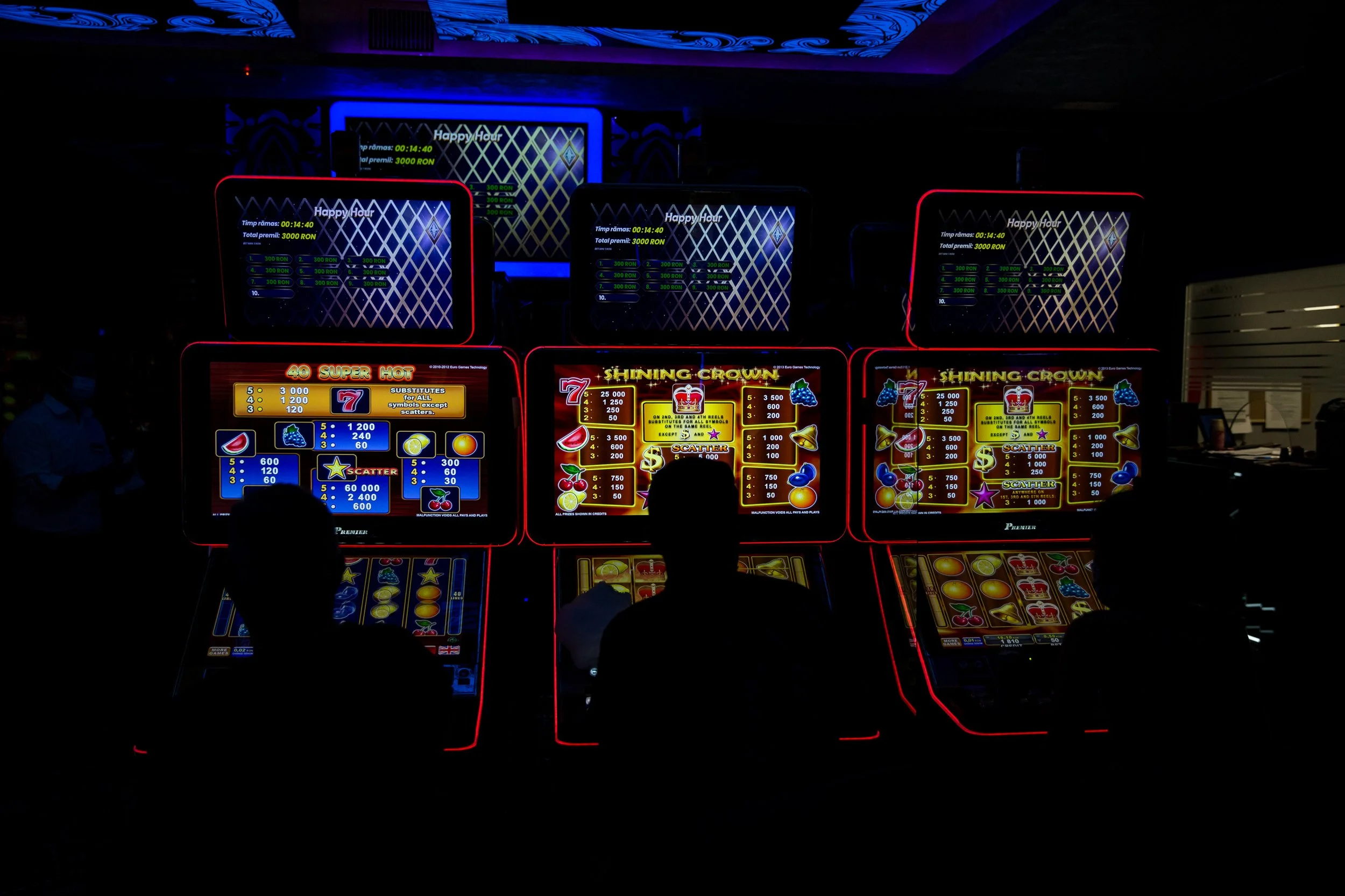 Photo of illuminated slot machines in a dark casino, with digital screens displaying game information and colorful graphics.