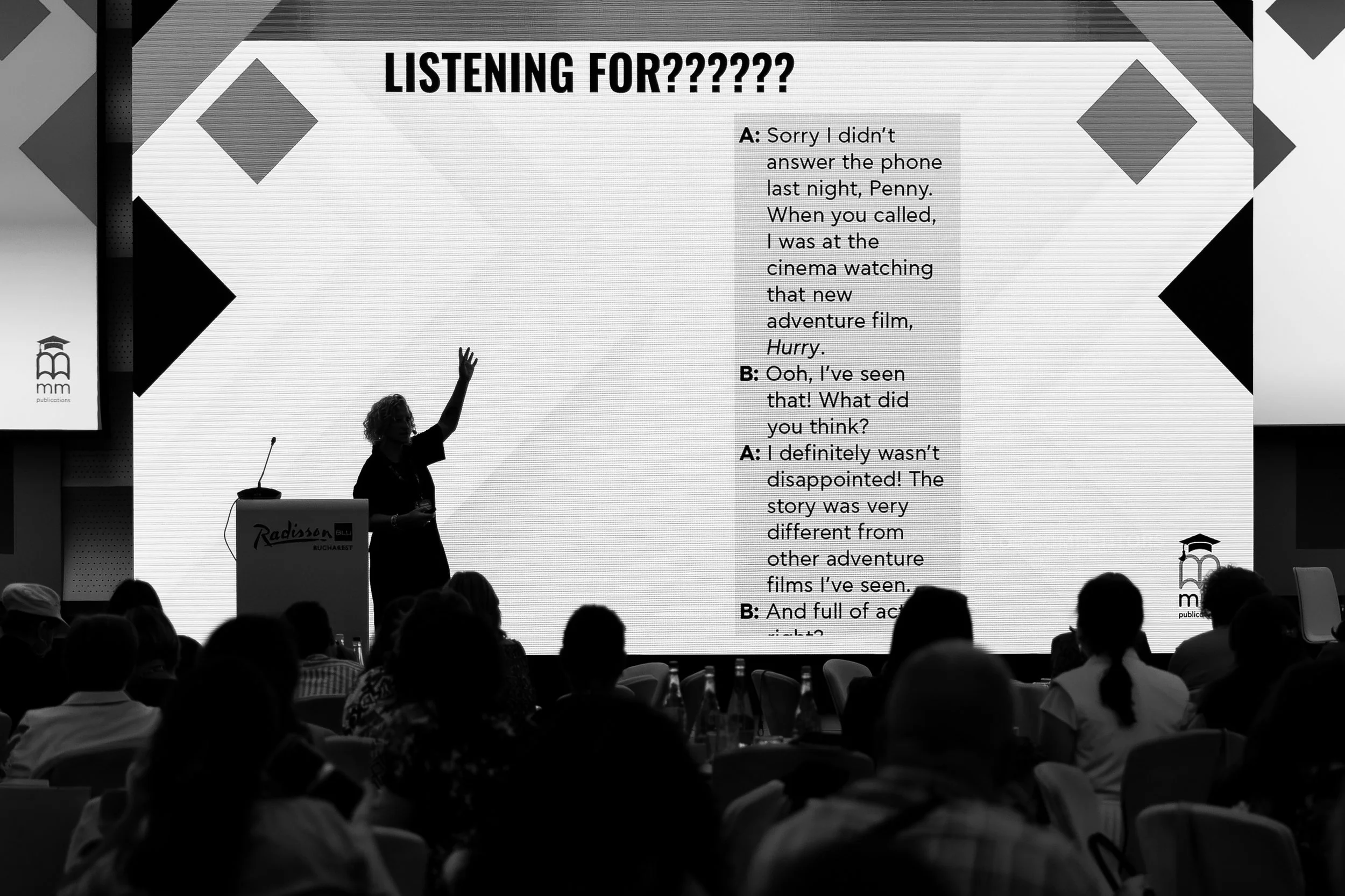 A woman giving a presentation in front of a large display screen at the Radisson Blu hotel in Bucharest. The screen displays a questionnaire titled 'Listening For?????' with dialogues about a missed phone call and a movie at the cinema. The audience 