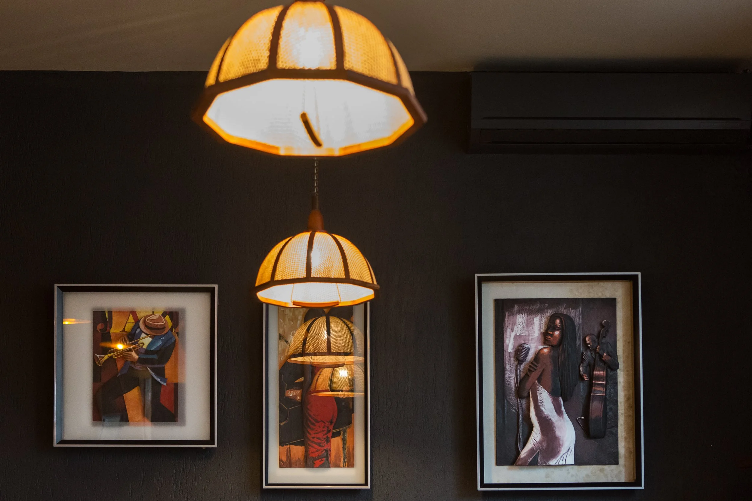 Multiple decorative hanging lamps with warm lighting in a room with framed artwork on a dark wall.
