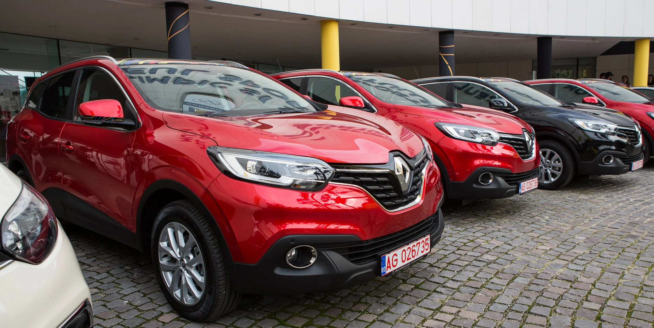 Row of red and black Renault cars parked outside a building with yellow pillars.