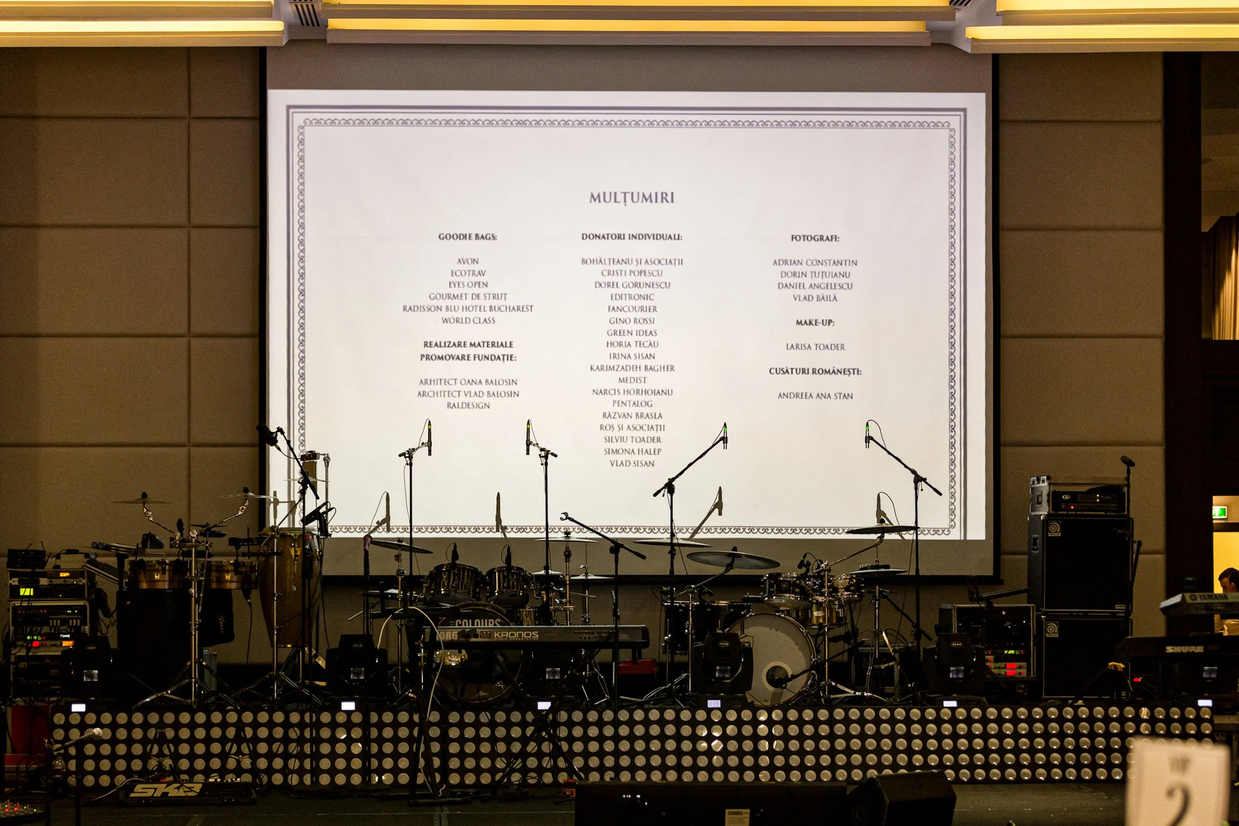 Stage setup with musical instruments, microphones, and equipment in front of a large screen displaying acknowledgment text in Romanian.
