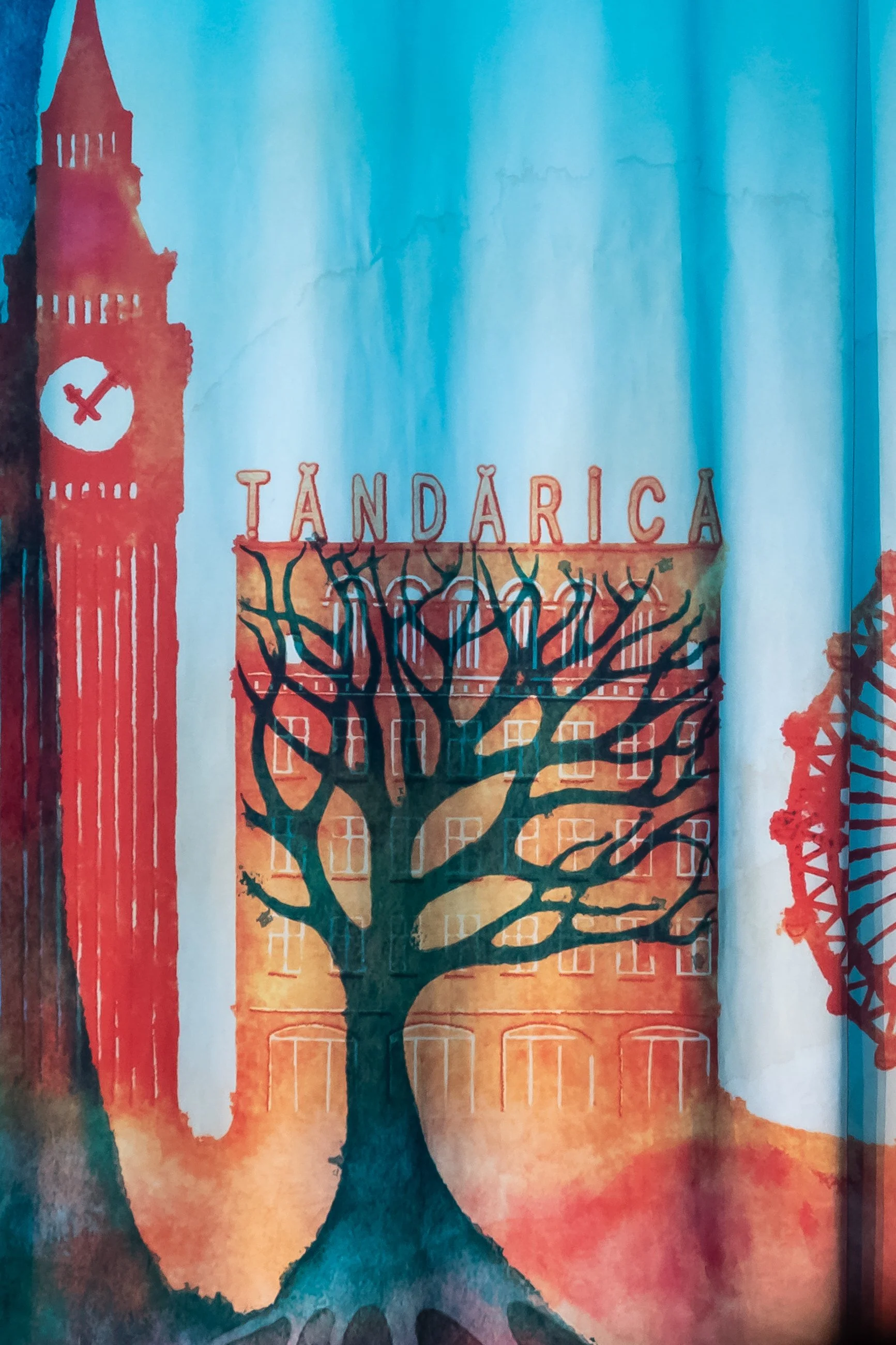 A watercolor painting of Big Ben, a tree, and a building with the word 'TANDÁRICA' in colorful letters. The sky and background are painted in shades of blue, orange, and red.