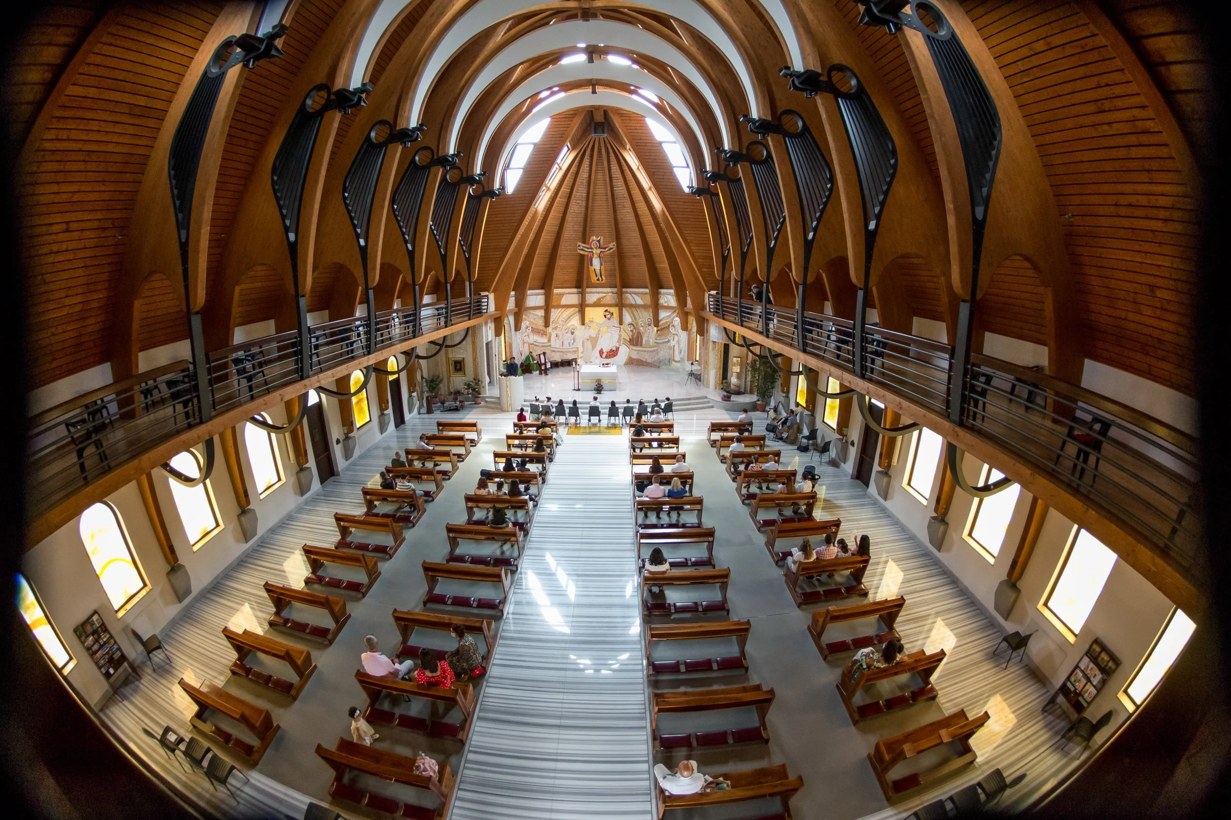Interior of a church or cathedral with wooden arches, stained glass windows, and pews filled with people.