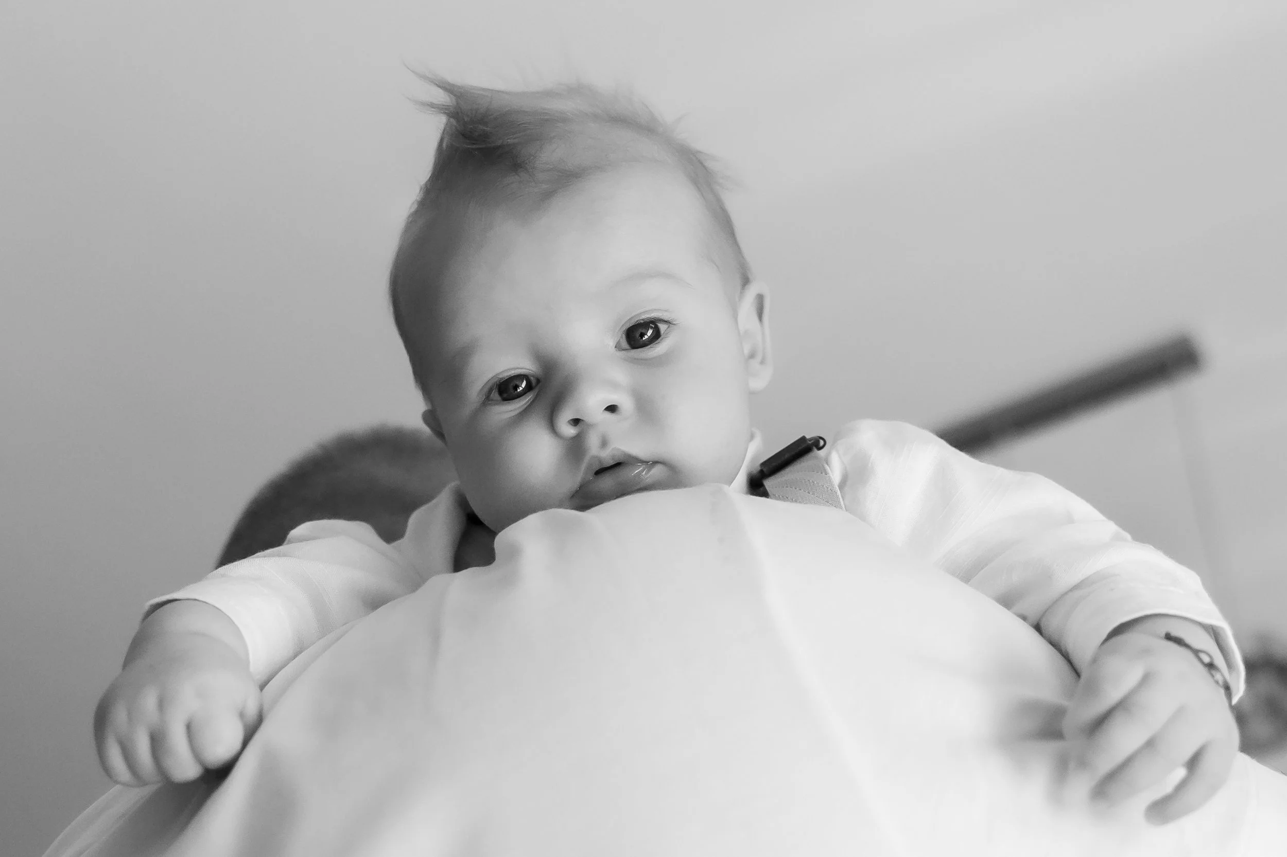A young child with short hair and light skin, lying on a person's chest, gazing directly at the camera, with a neutral gray background.