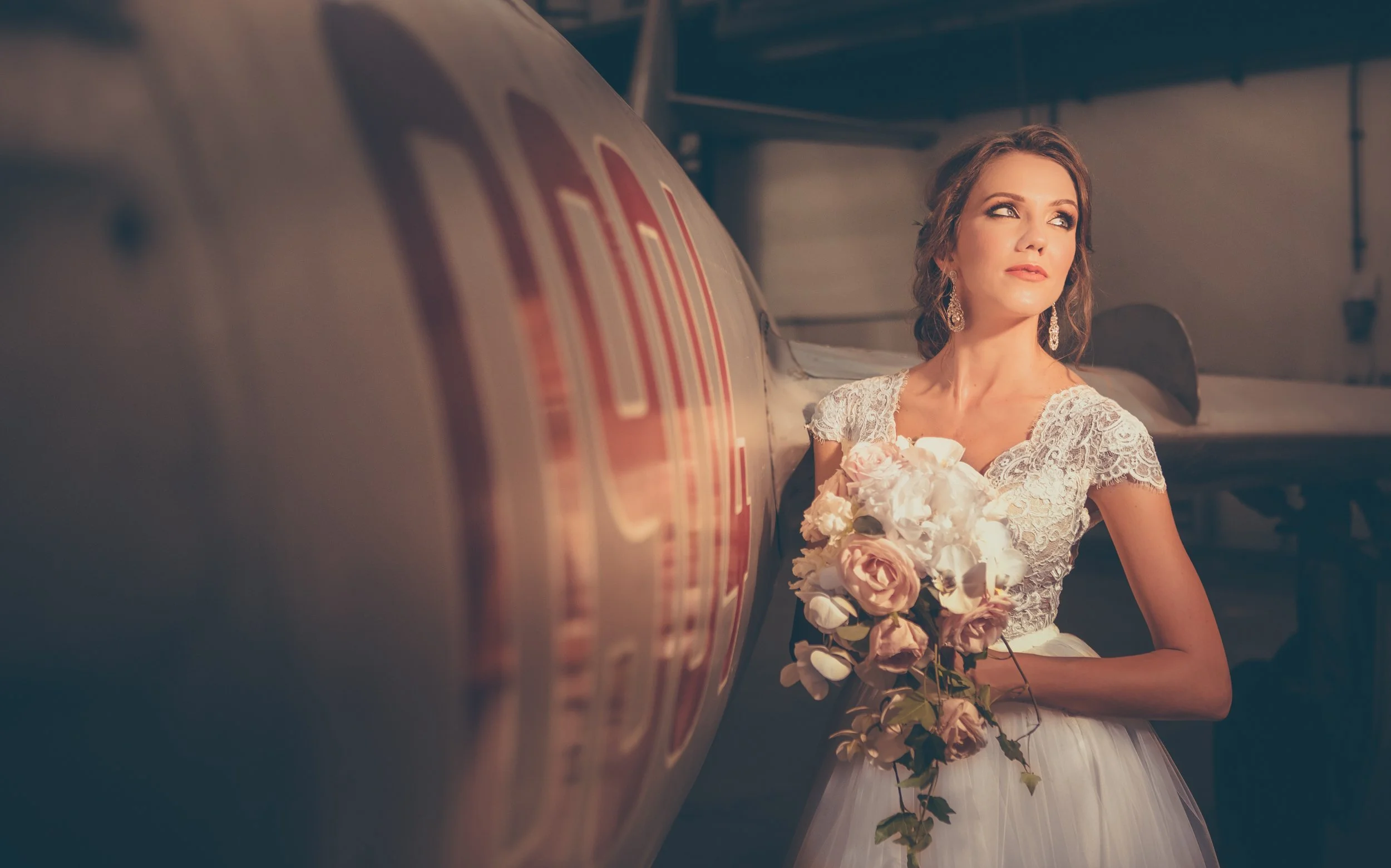 A woman in a wedding dress holding a bouquet of flowers, standing near an airplane.
