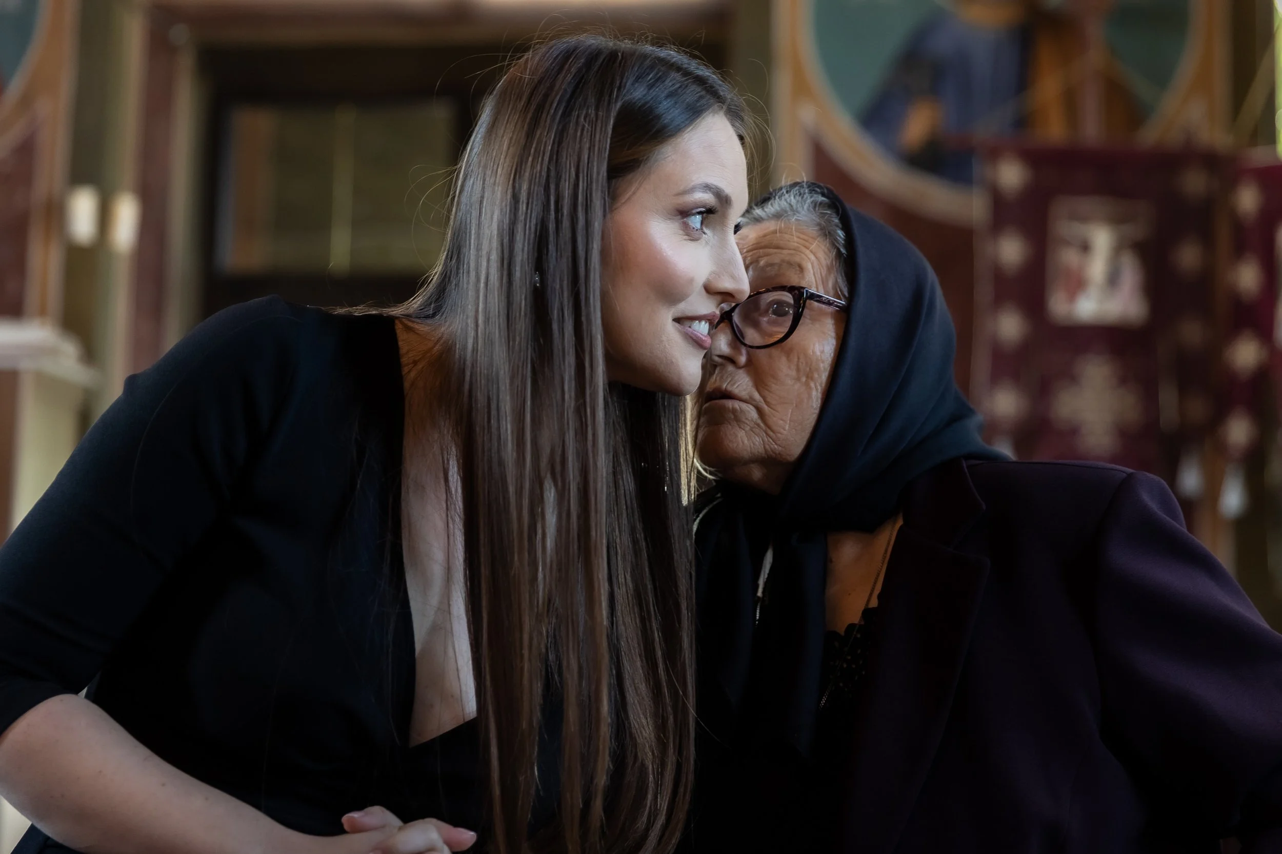A woman with long brown hair and a man wearing glasses and a hoodie, leaning in close and touching foreheads in an intimate moment.