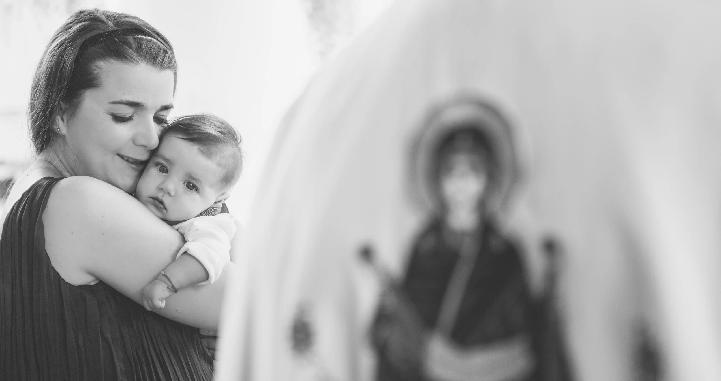 A woman with her eyes closed smiling as she hugs a young child in her arms, both appearing happy and affectionate, in a black and white photo.
