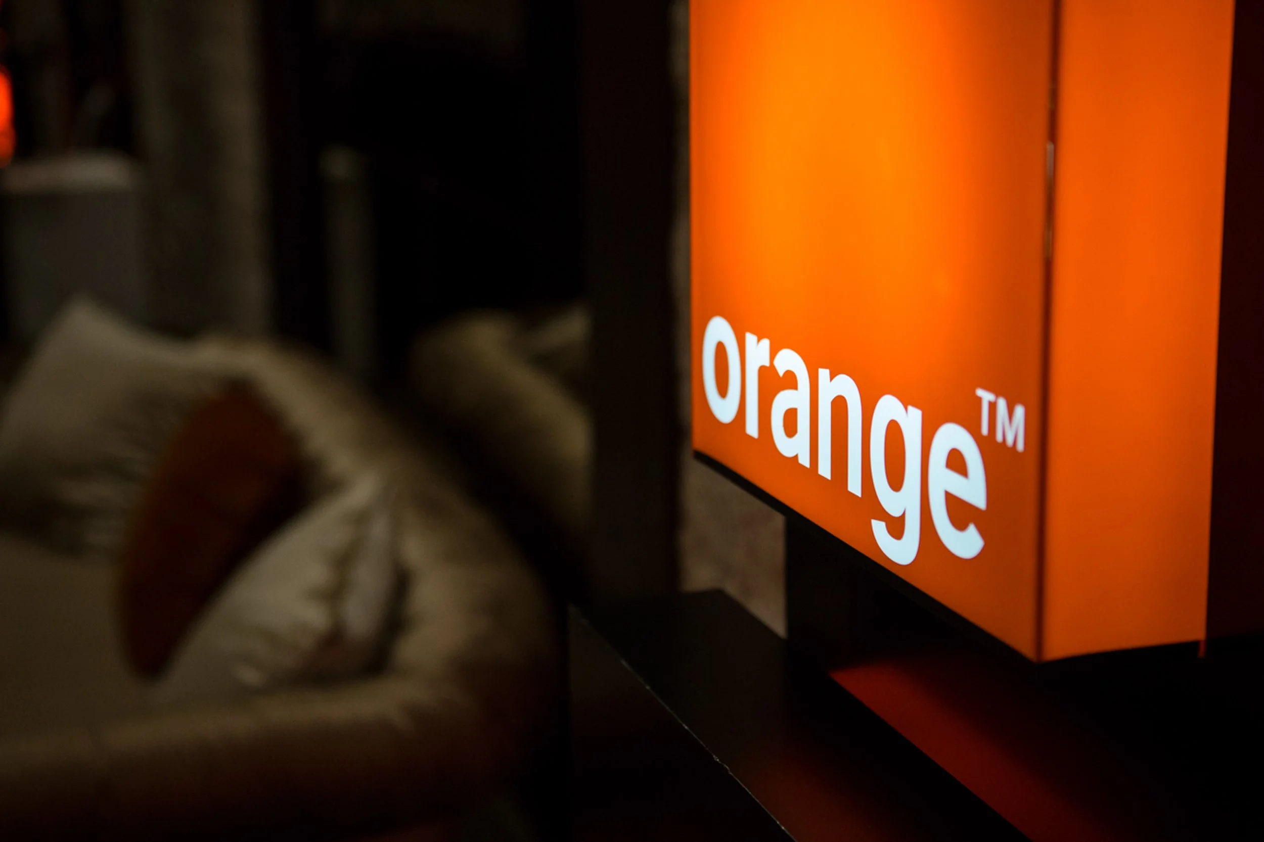 Close-up of a hand reaching towards an orange illuminated display reading 'Orange'.