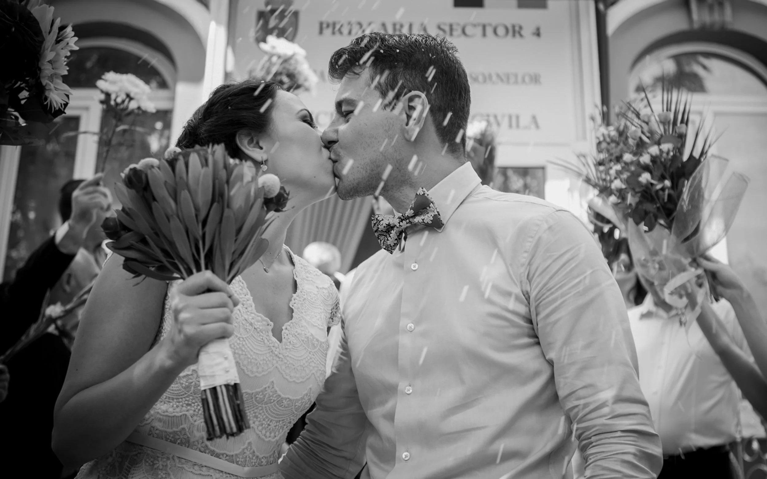 A newlywed couple sharing a kiss, surrounded by flowers and confetti, during their wedding celebration.