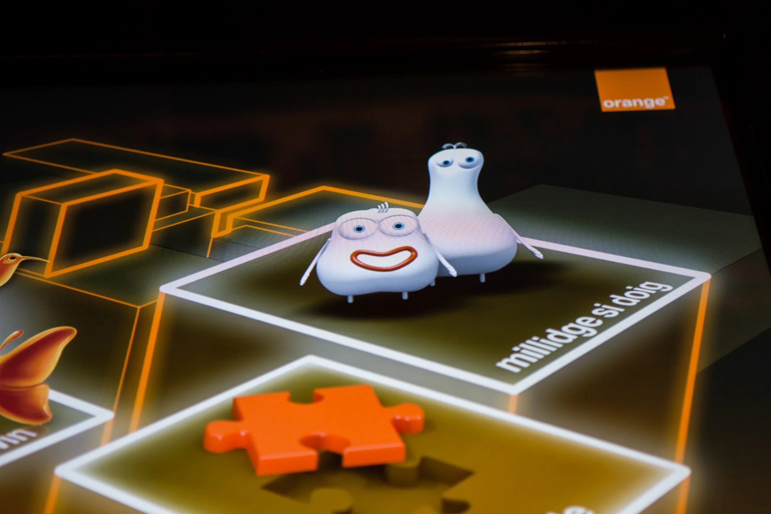 Animated characters resembling garlic bulbs with facial features, arms, and legs on a game board, with the orange 'orange' logo in the top right corner.