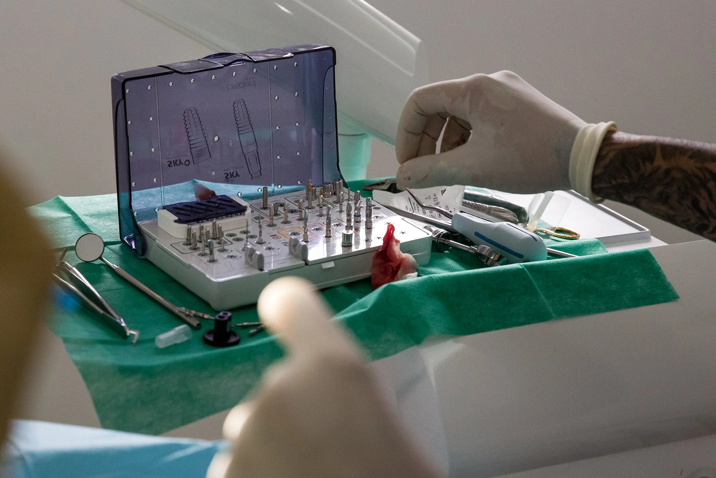 A medical professional handling surgical equipment on a sterile green drape, with a tray of surgical instruments and tools visible.