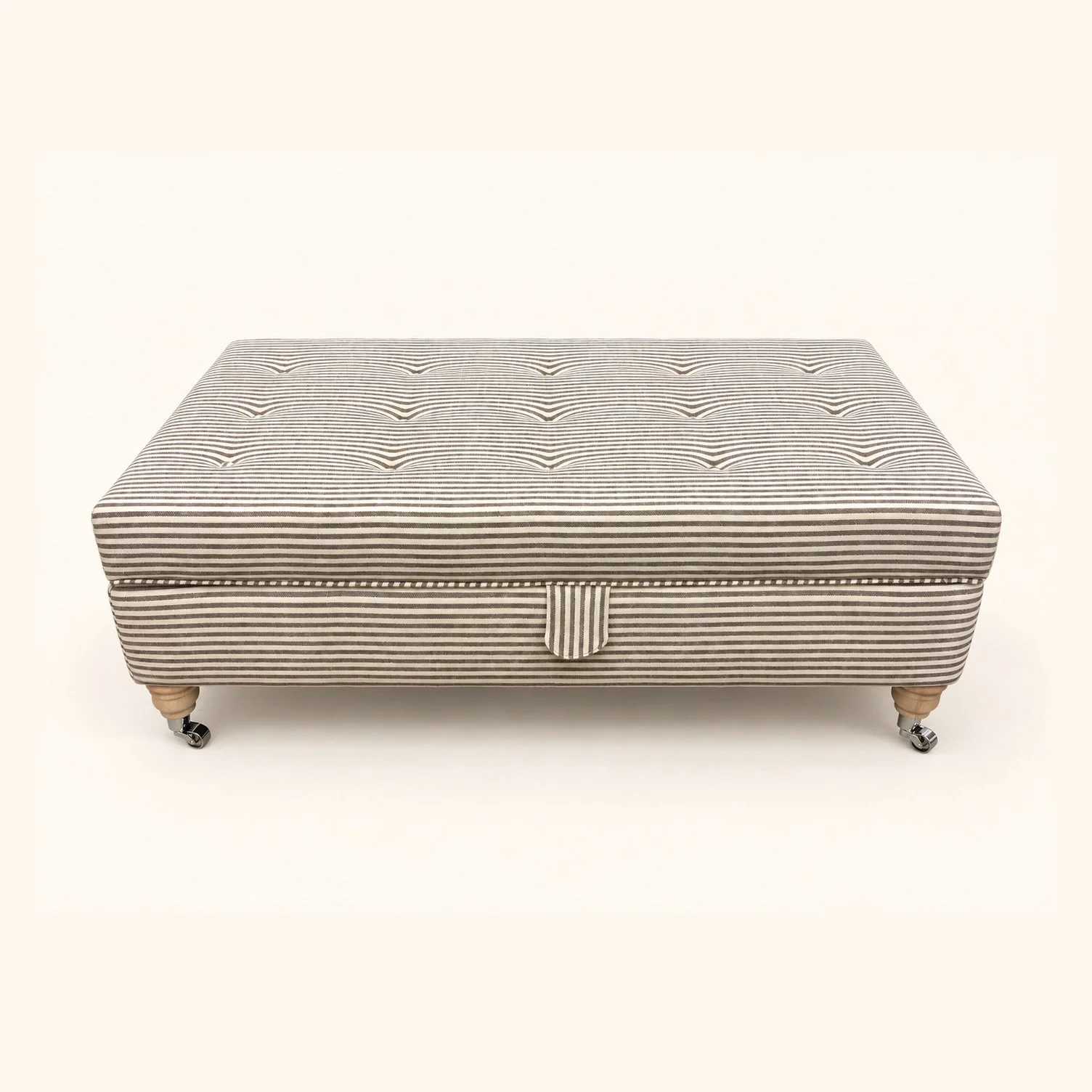 Before reupholstery: rectangular storage ottoman in finely striped fabric, with a buttoned top, front pull tab and wooden feet.