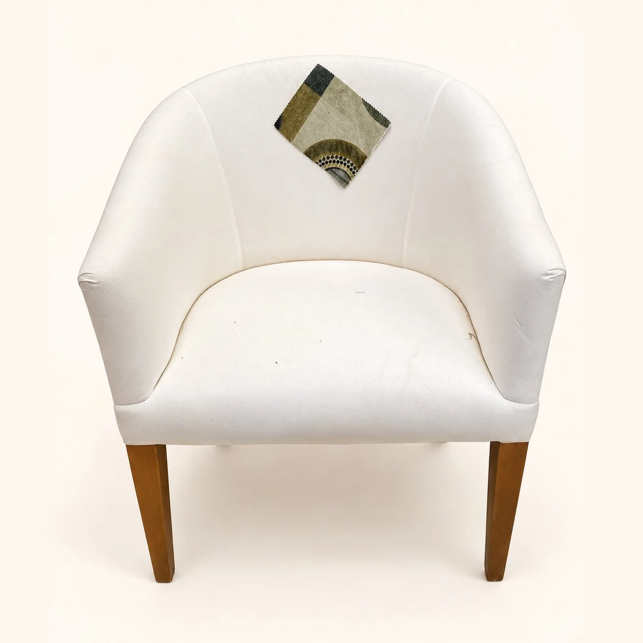 Before reupholstery: a compact tub chair in plain white fabric, with a rounded back, integrated arms and tapered wooden legs.