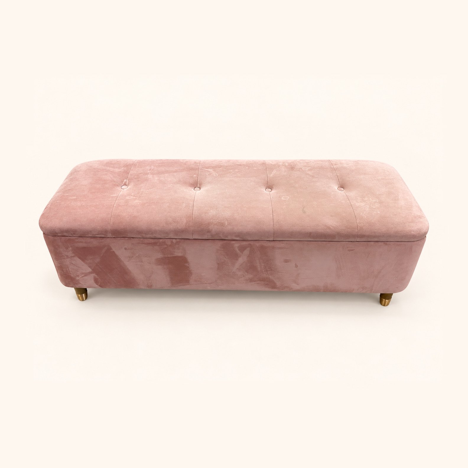 Before reupholstery: a long pale pink ottoman with a buttoned top and small wooden feet.