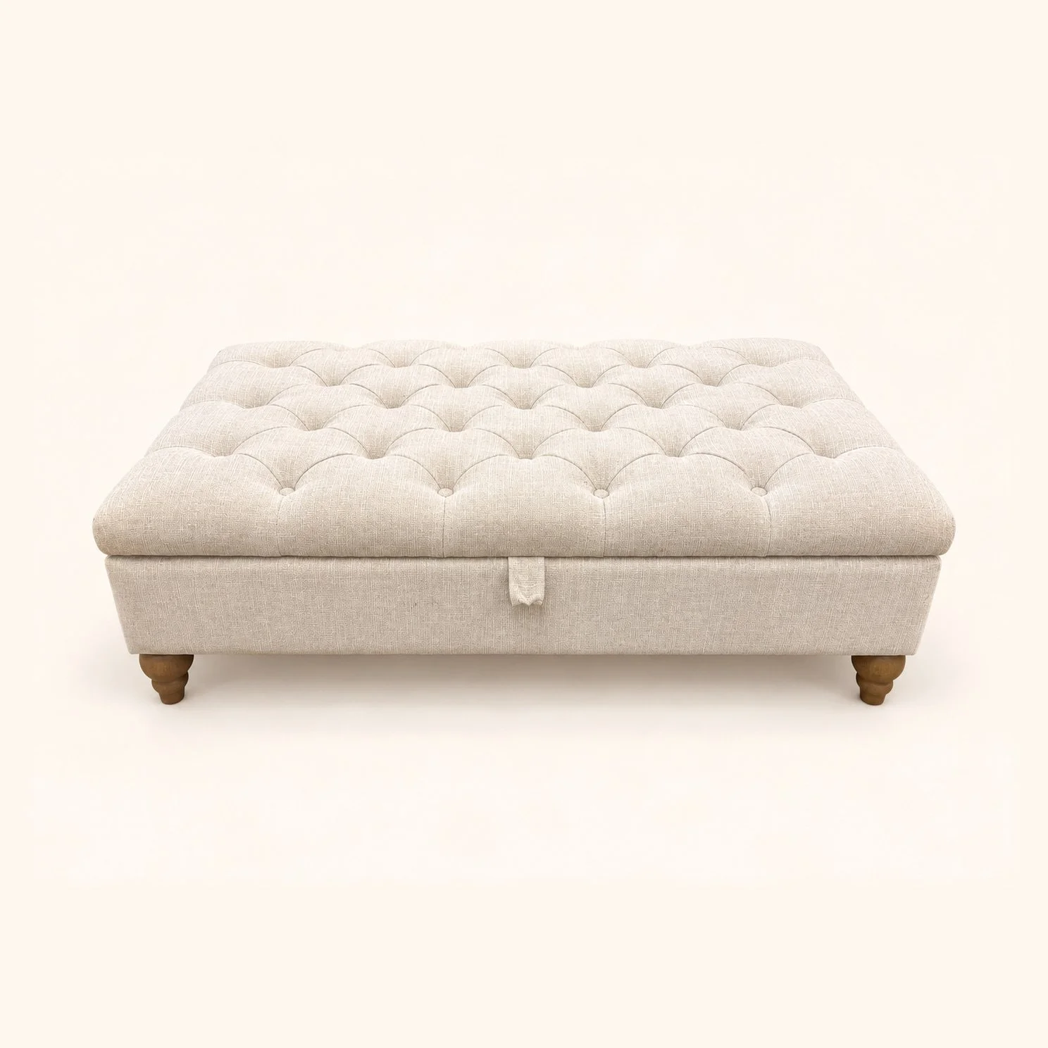 After reupholstery: rectangular storage ottoman in cream fabric with a deep-buttoned top, front pull tab and wooden feet.