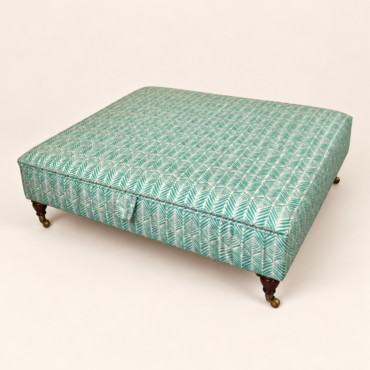 After reupholstery: ottoman in teal patterned fabric with dark wooden feet and castors