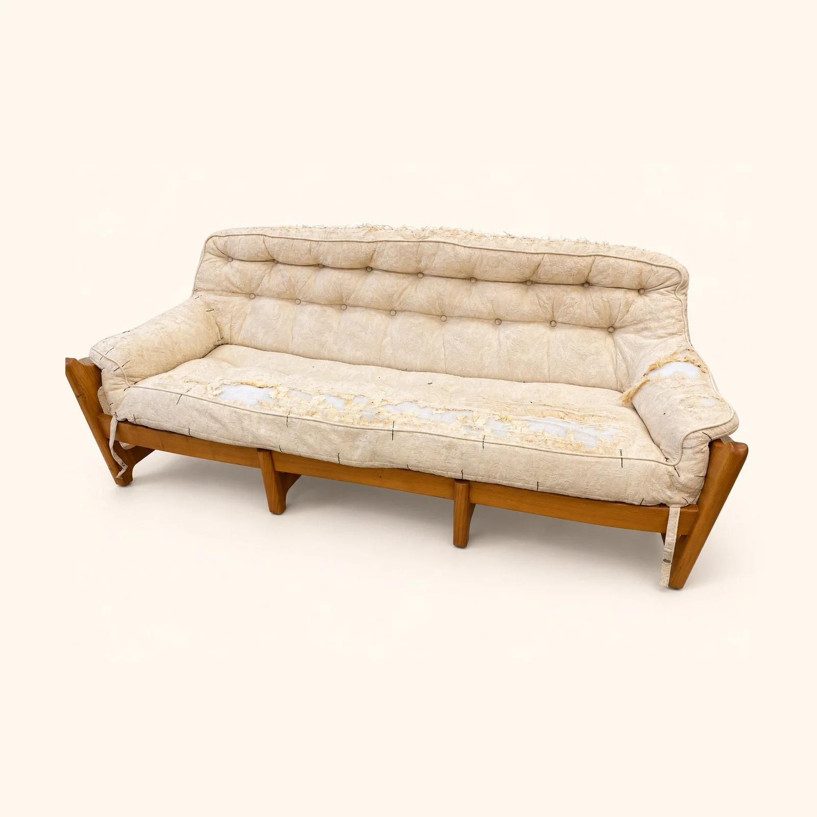 Before reupholstery: a wooden-frame sofa in worn cream fabric, with a tufted back, shaped sides and tapered wooden legs.