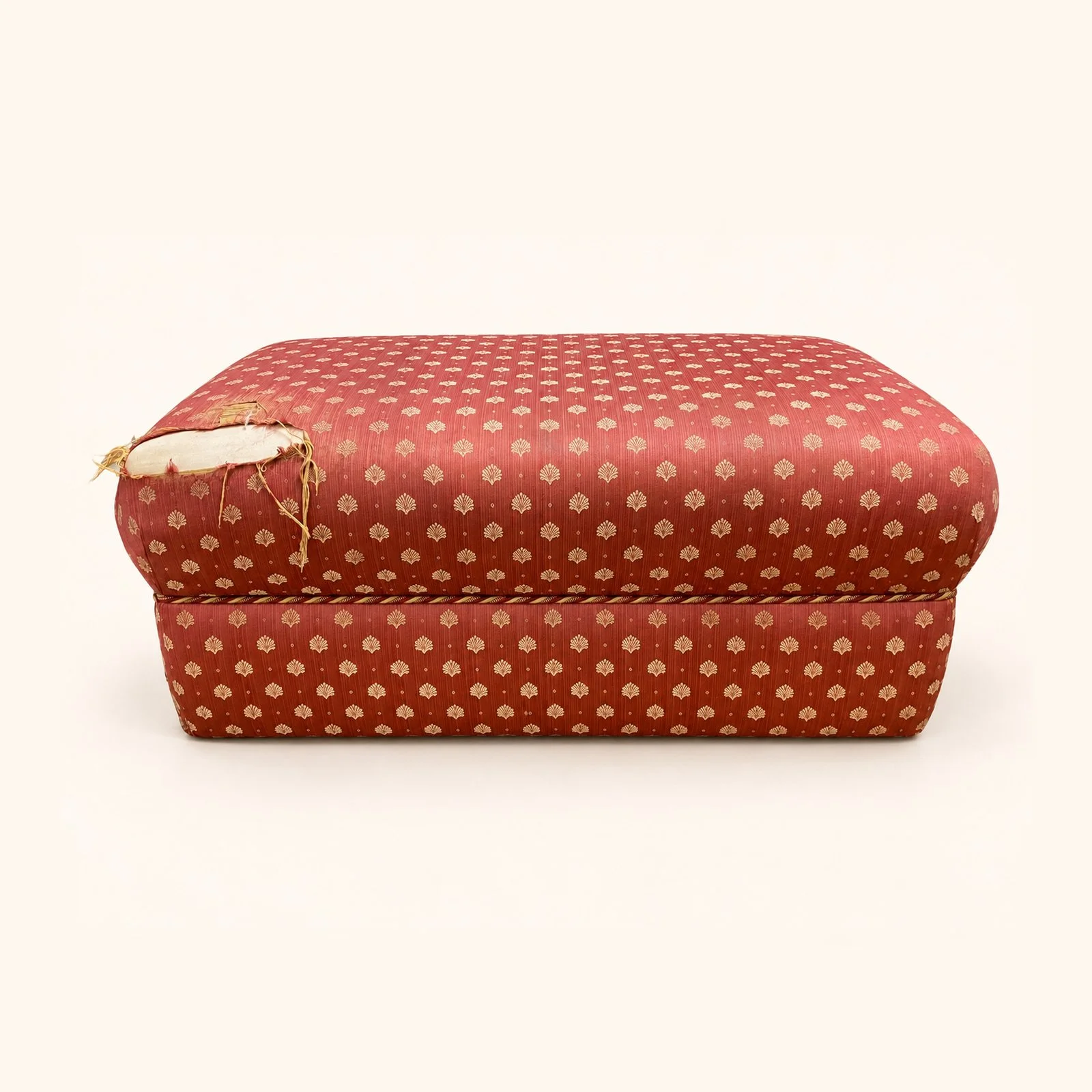 Before reupholstery: a rectangular ottoman in worn red patterned fabric, with a rounded padded lid.