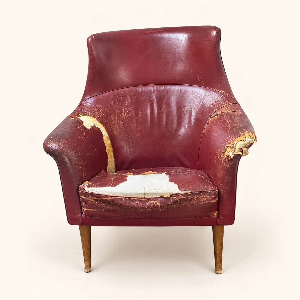 Before reupholstery: a worn burgundy armchair with torn upholstery on the arms and seat, a high curved back and tapered wooden legs.