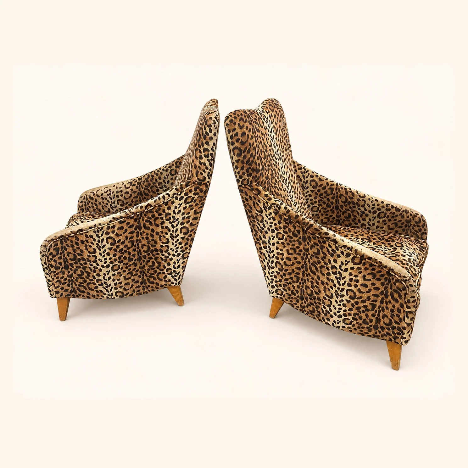 Before reupholstery: a pair of tall high-back chairs in animal-print fabric, with sloping arms and tapered wooden legs.