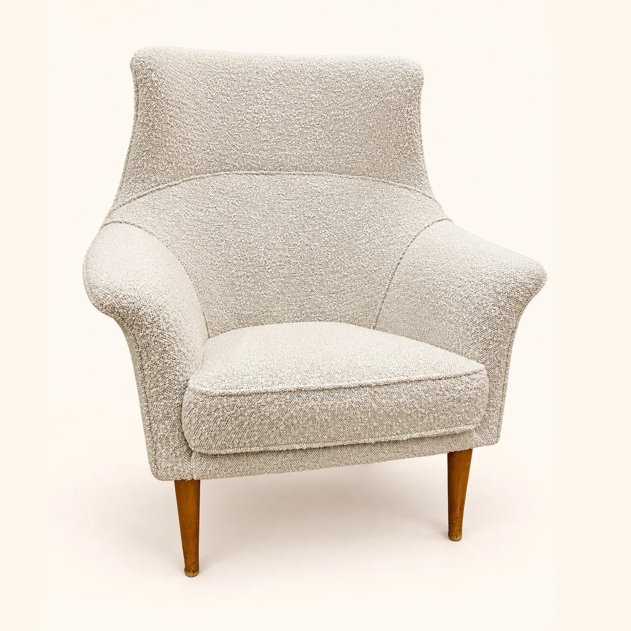 After reupholstery: an armchair in cream textured fabric, with a high curved back, shaped arms and tapered wooden legs.