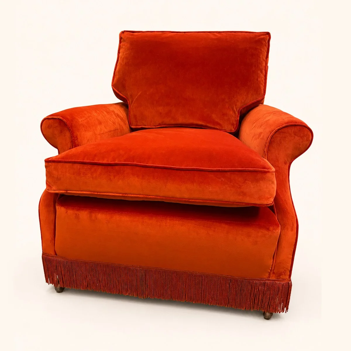 After reupholstery: orange upholstered armchair with rounded arms, a loose seat cushion and a fringed base.