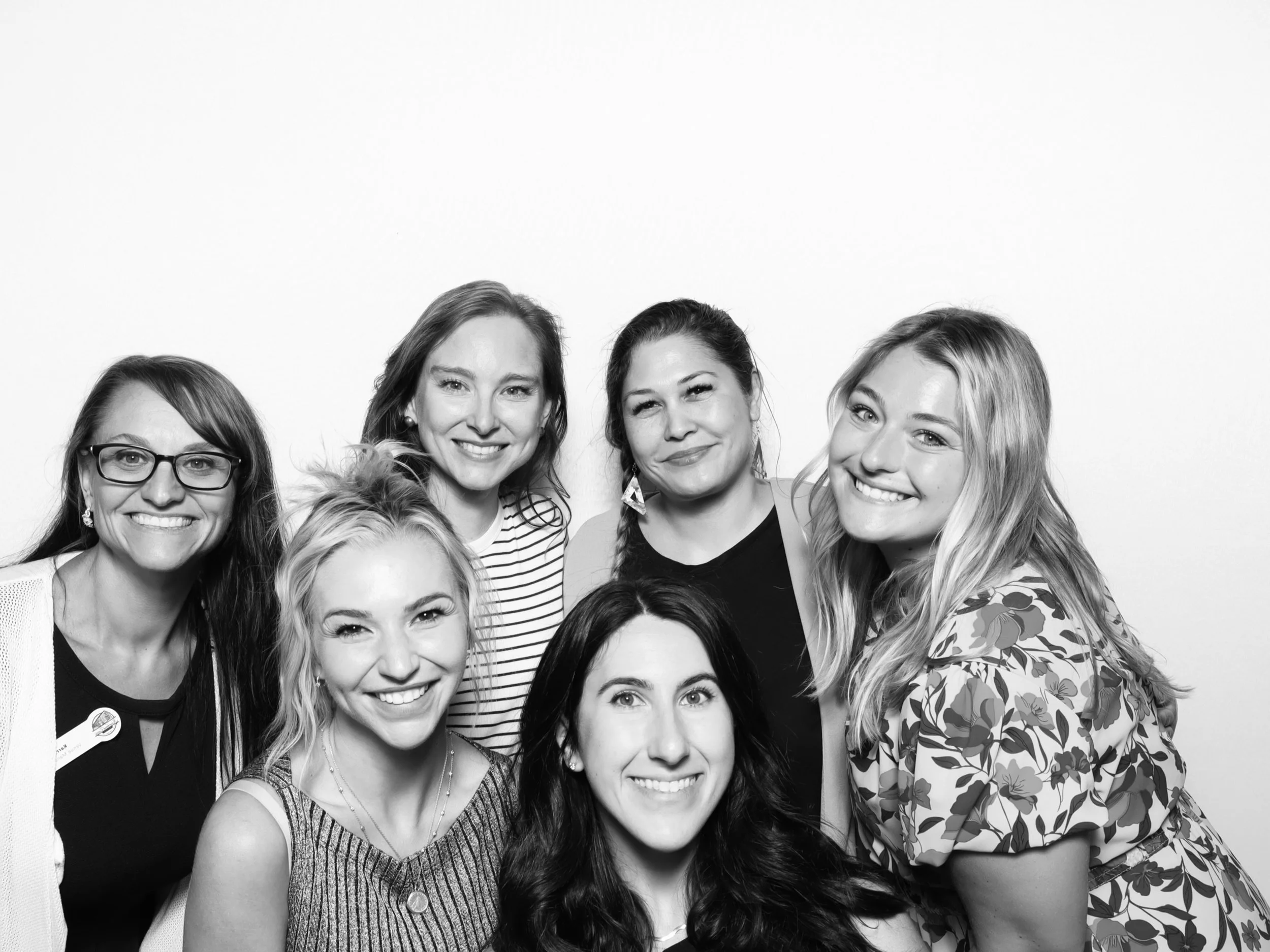 Group of women smiling and posing together against a plain background, black-and-white photo.