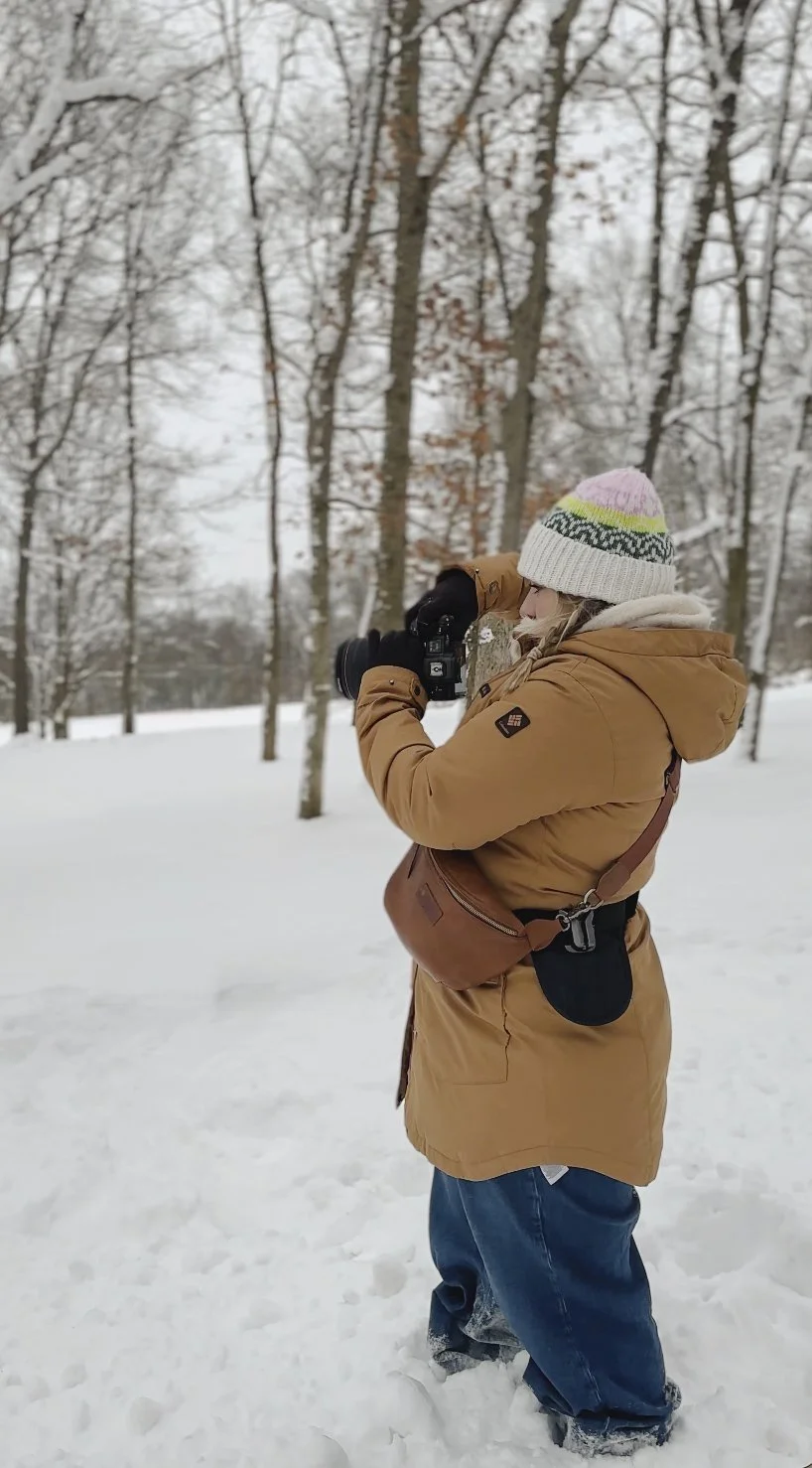 Person in winter clothing taking a photograph with a camera in a snowy forest.