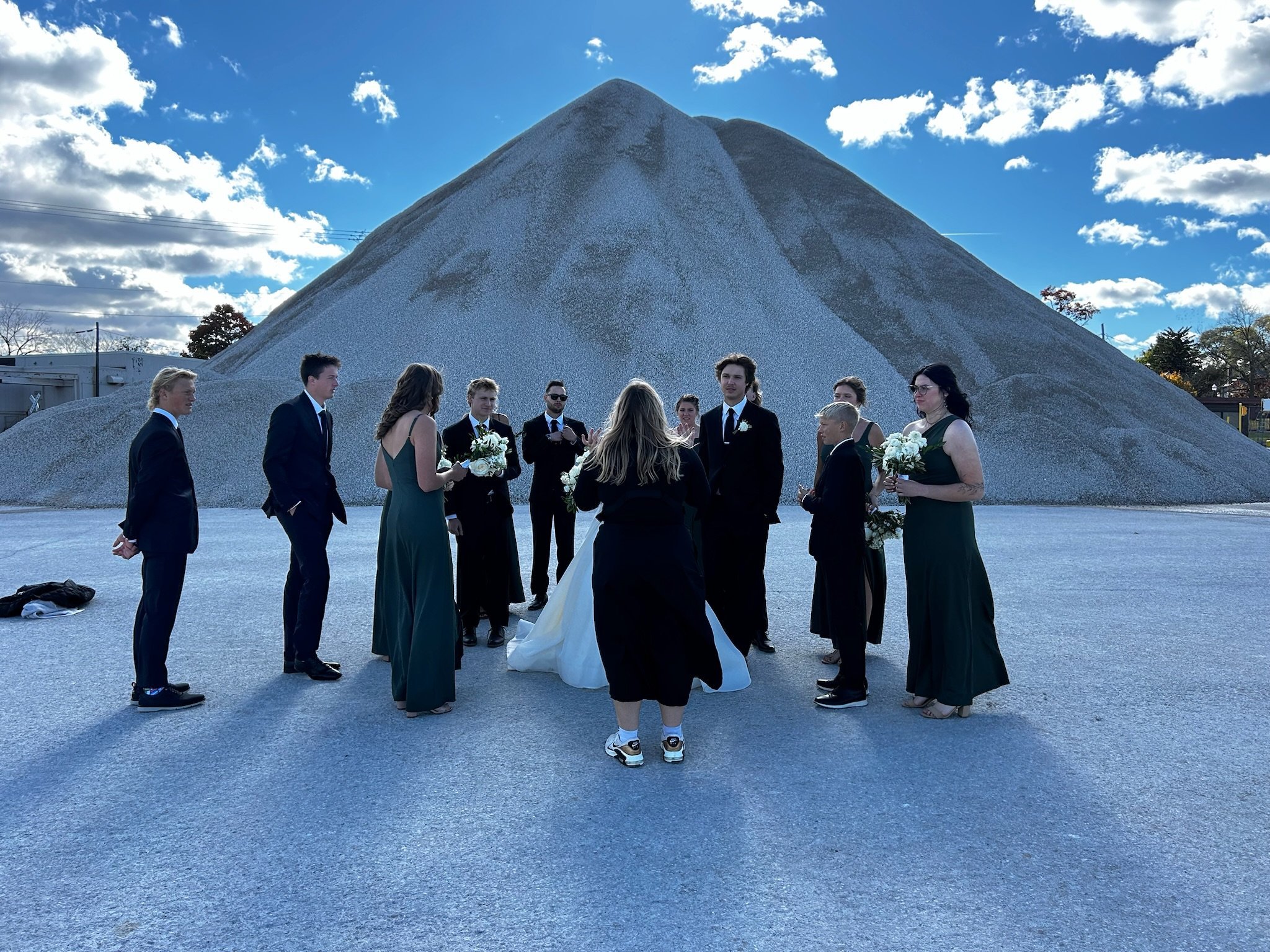 A group of people dressed in formal attire gathered in a circle outdoors with a mountain in the background, involving a ceremony or celebration.