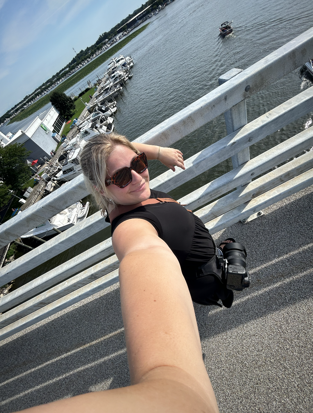 A woman taking a selfie on a bridge overlooking a marina with boats and water.