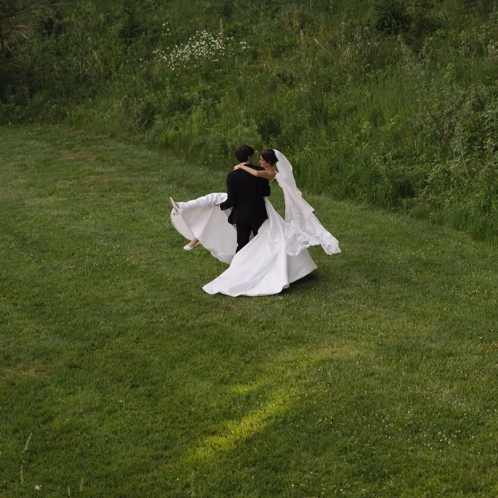 Bride and groom dancing on a grassy field with lush greenery in the background.