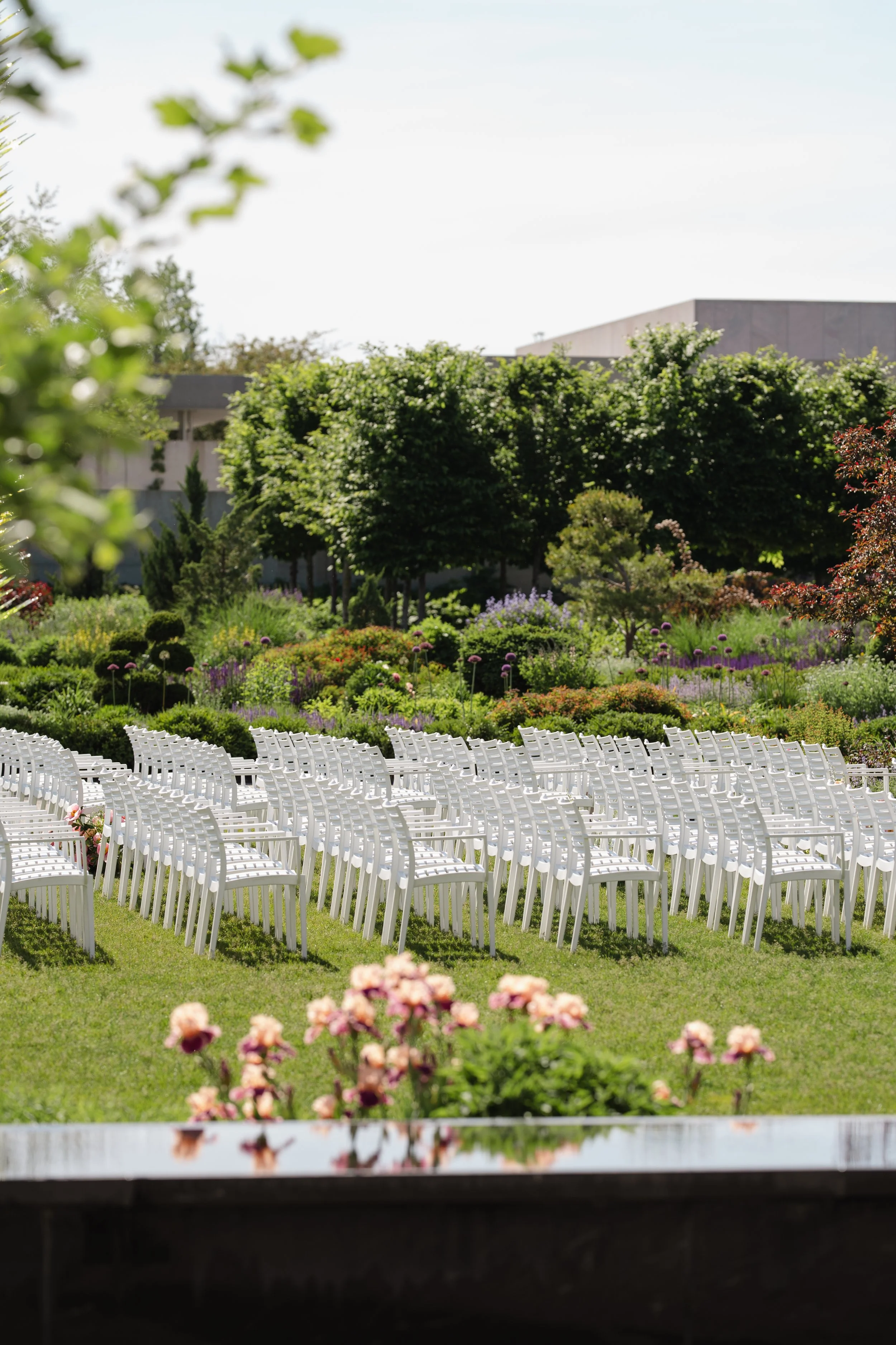 Empty chairs arranged for an outdoor wedding ceremony, with a garden and trees in the background.