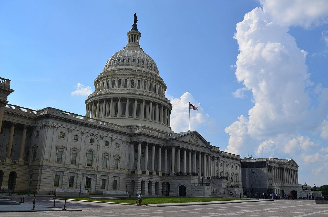 Capitol building with dome, columns, and American flag, under partly cloudy sky.