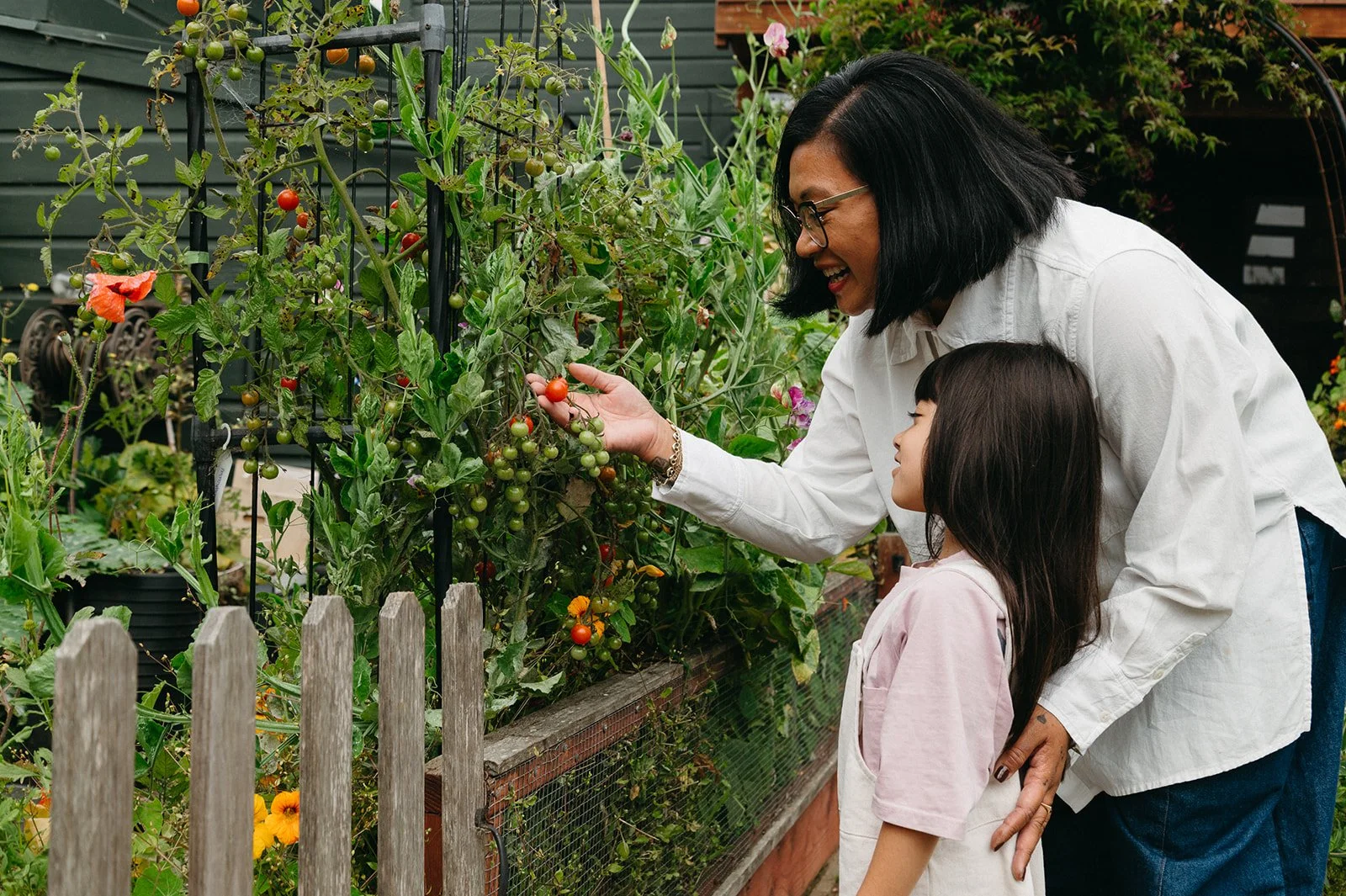 Root Founder, Michelle San Agustin in a garden smiling and holding a tomato plan with arm around daughter